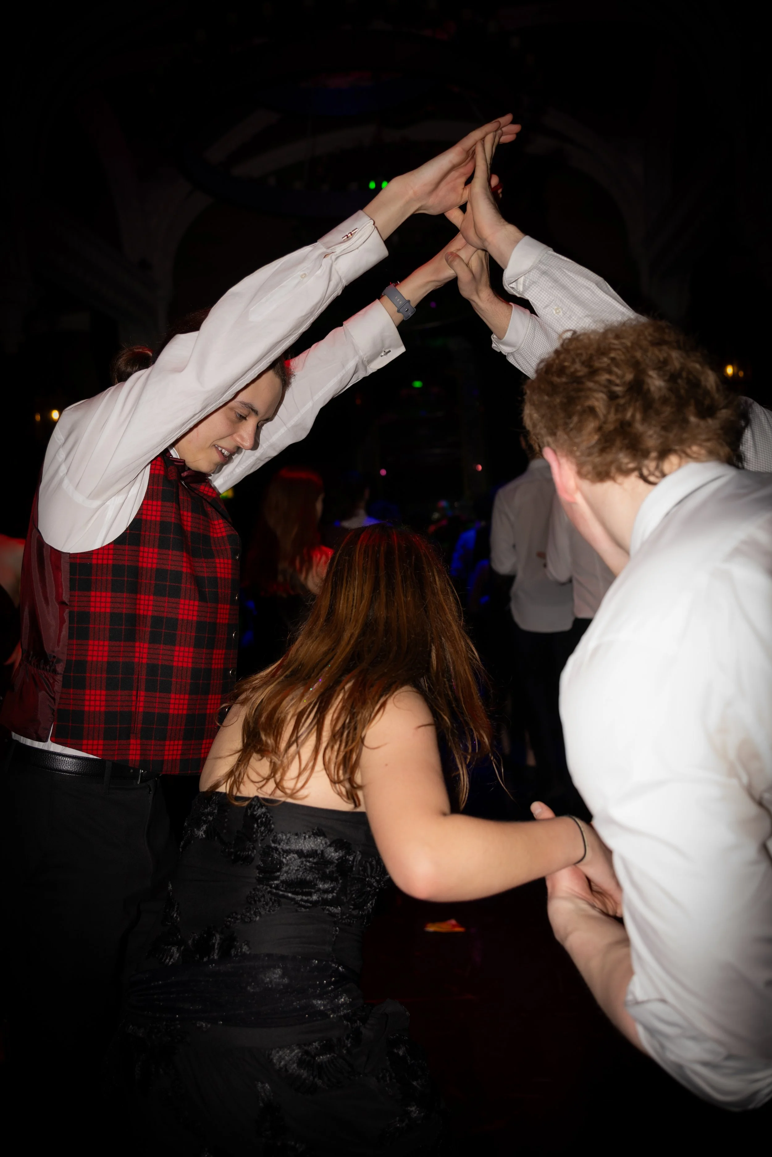 People dancing together in a dark room with with hands raised high in a team dance move.