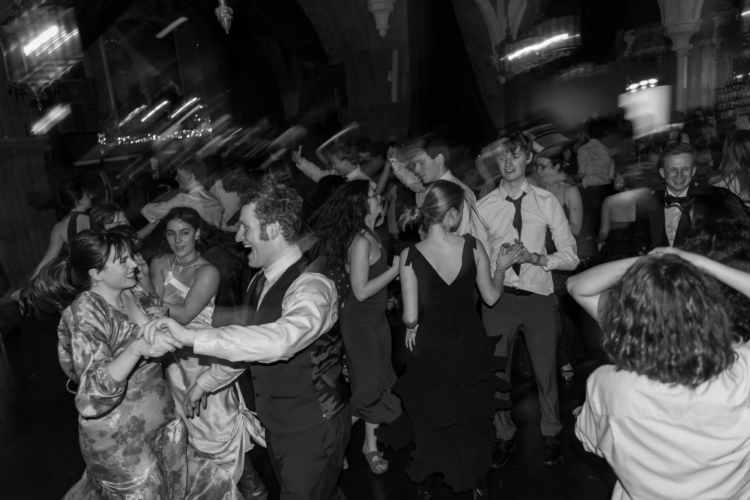 People dancing and socializing at a lively event or party in a large hall with ornate architecture.
