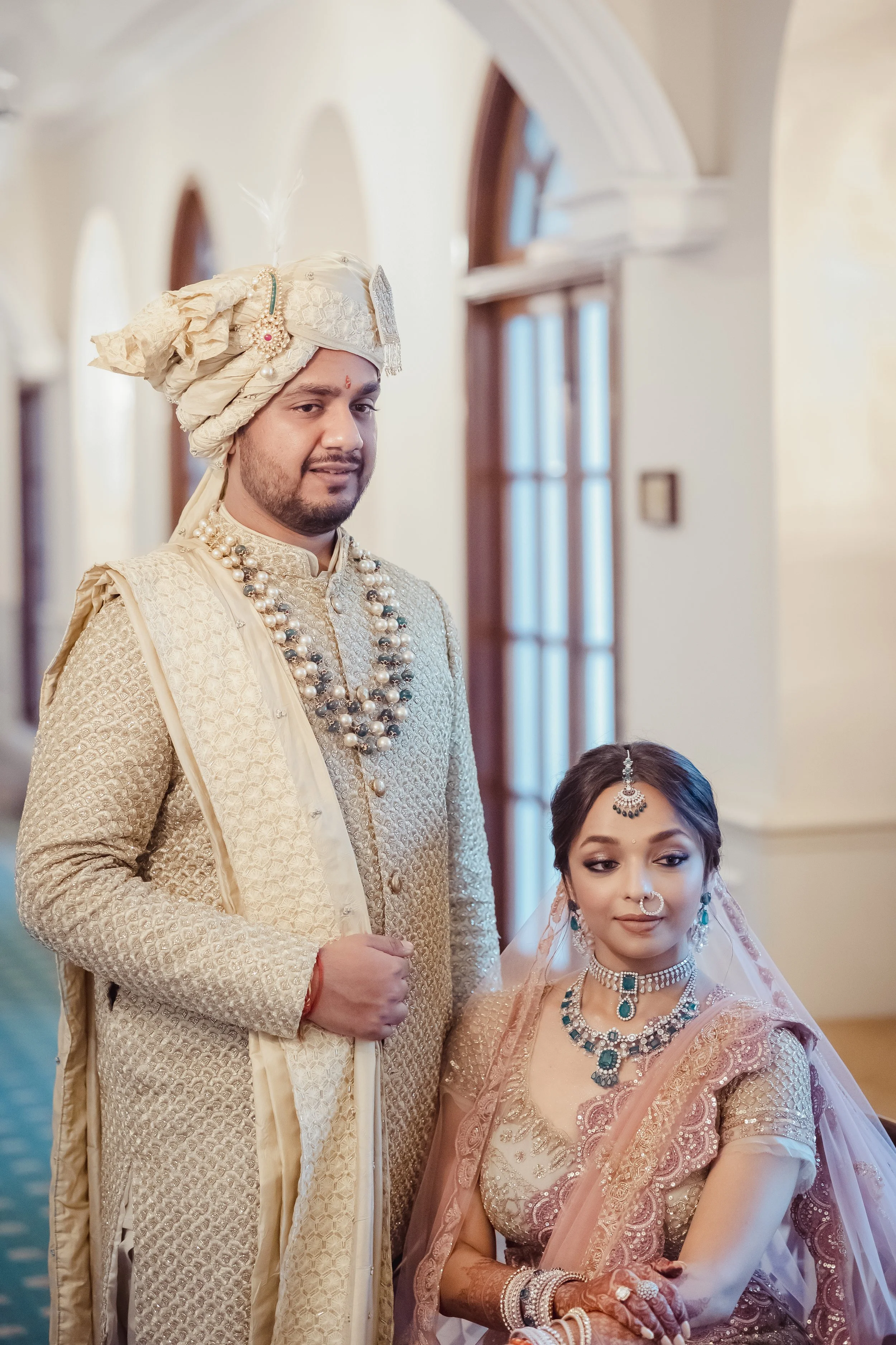 An Indian bride and groom dressed in traditional wedding attire indoors.
