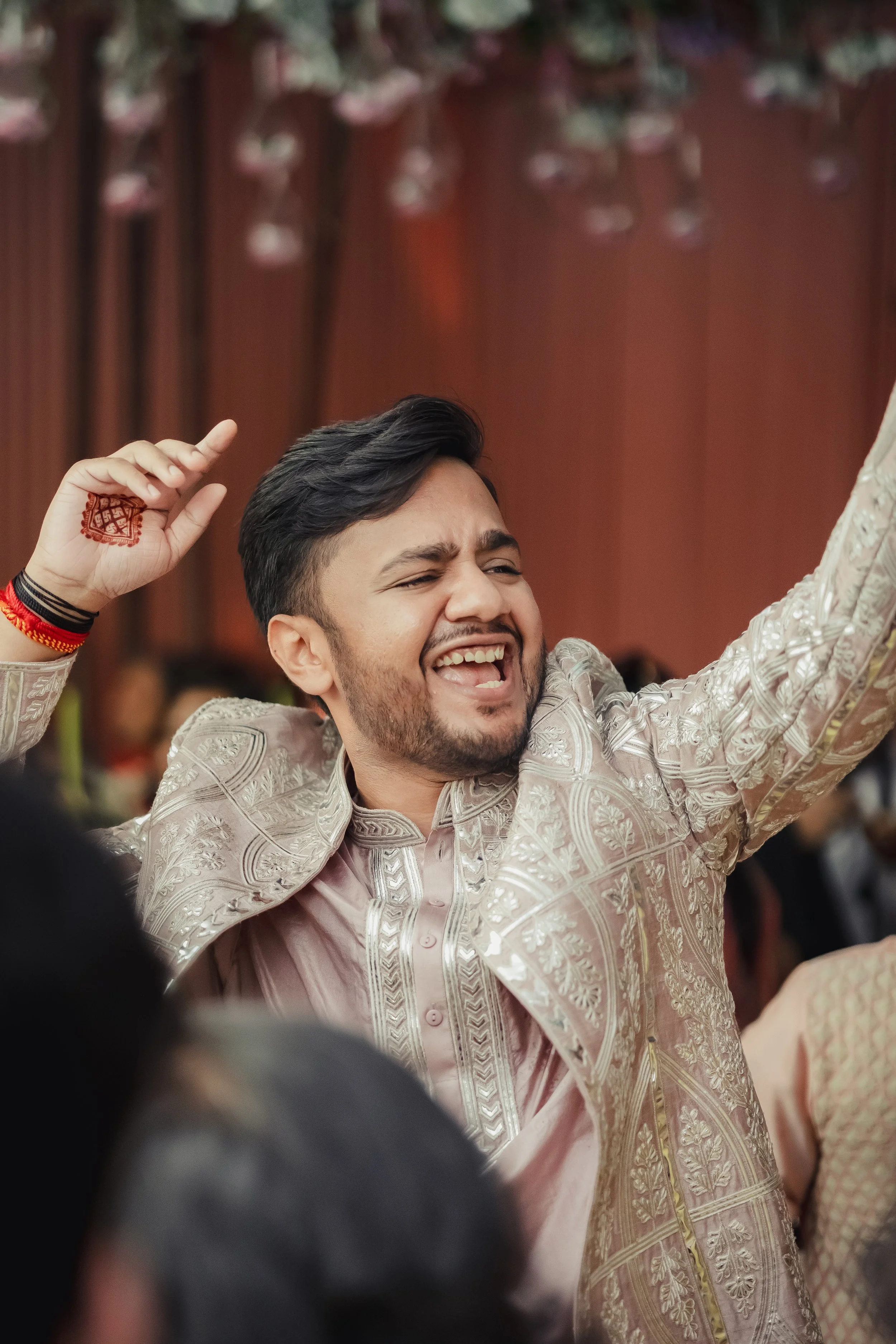 A man in traditional Indian attire, smiling and celebrating, with his arms raised, at a festive event.