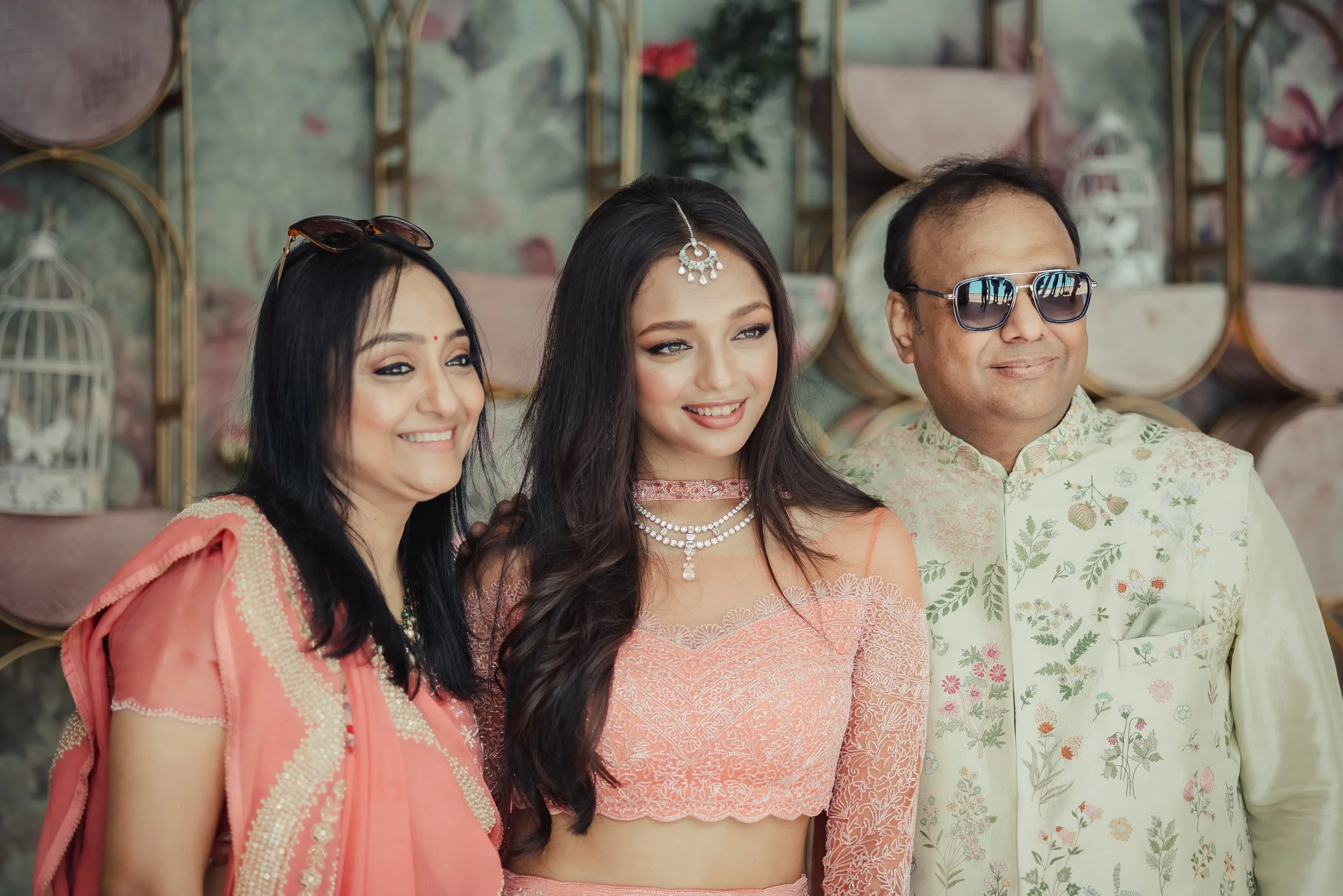 Three people smiling, dressed in traditional Indian attire, at a festive celebration.