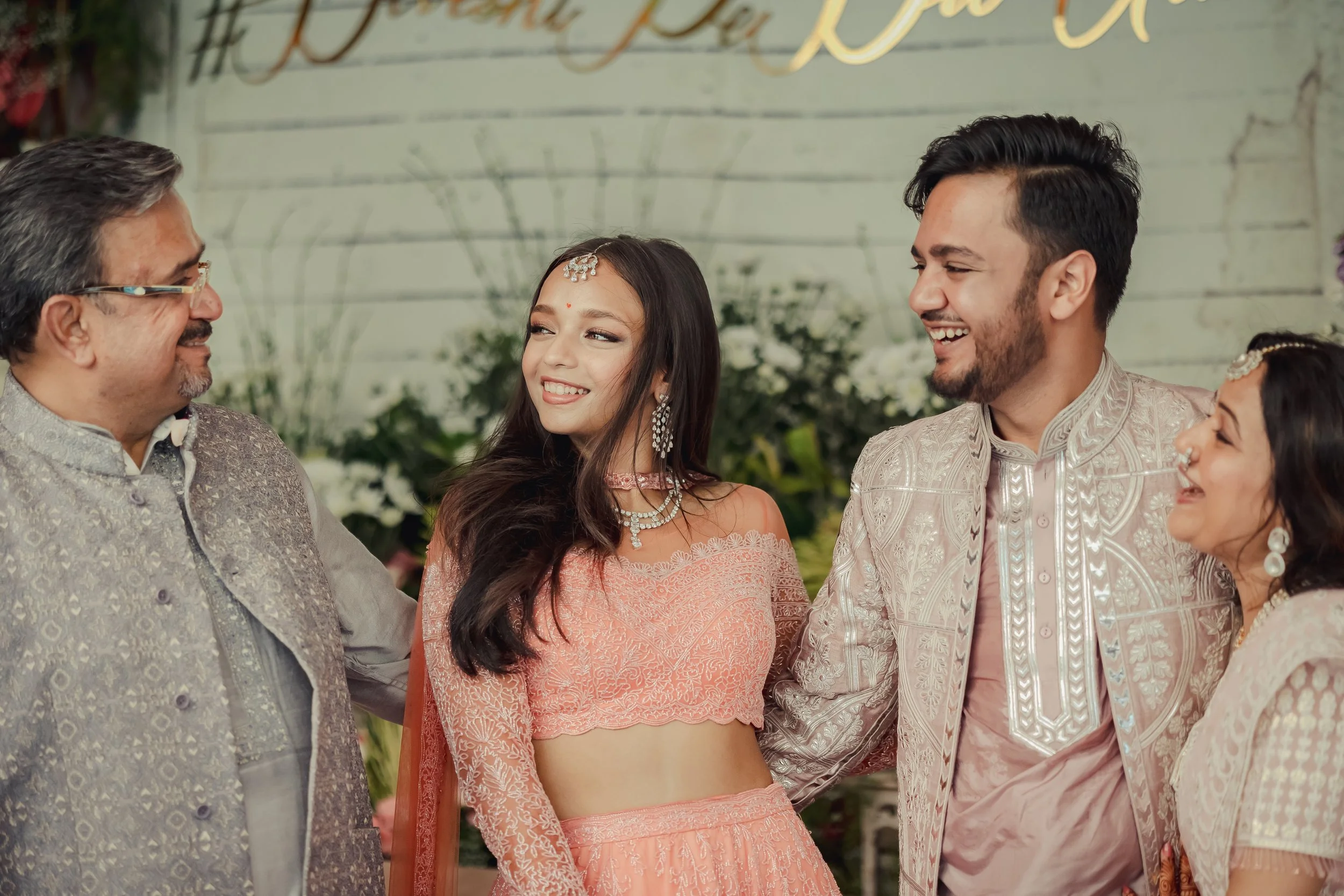 A group of Indian people dressed in traditional attire, smiling and interacting at a wedding celebration.