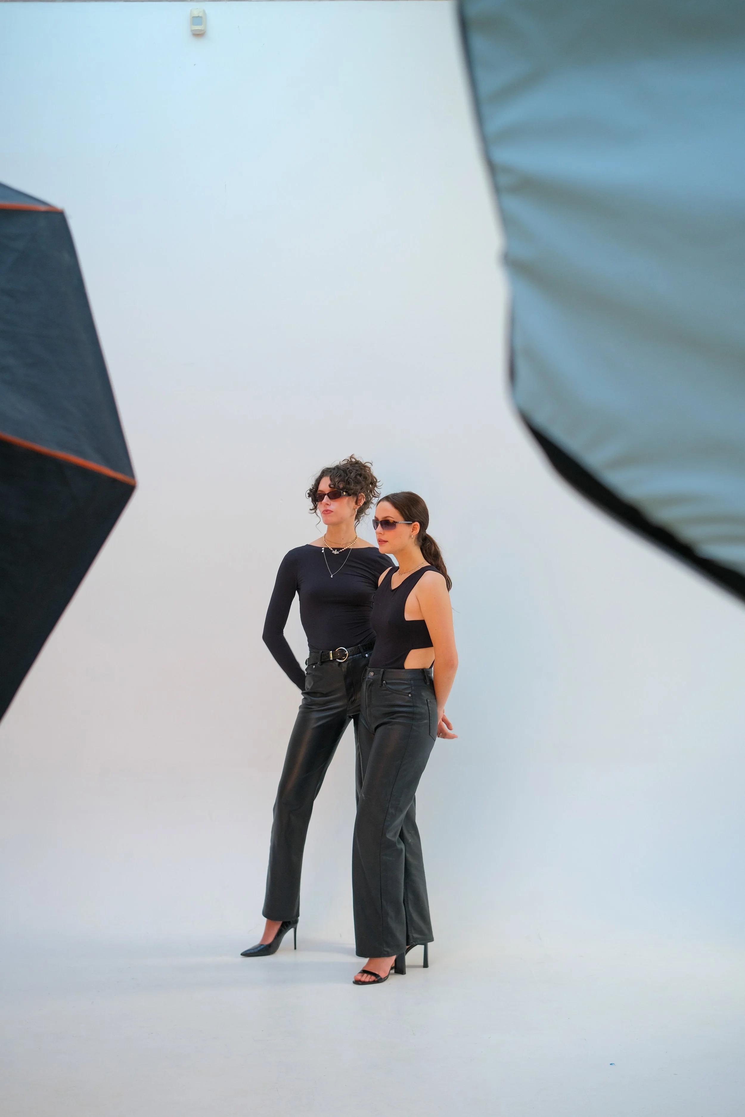 Two women posing for photographs in a studio with photography equipment visible in the foreground.