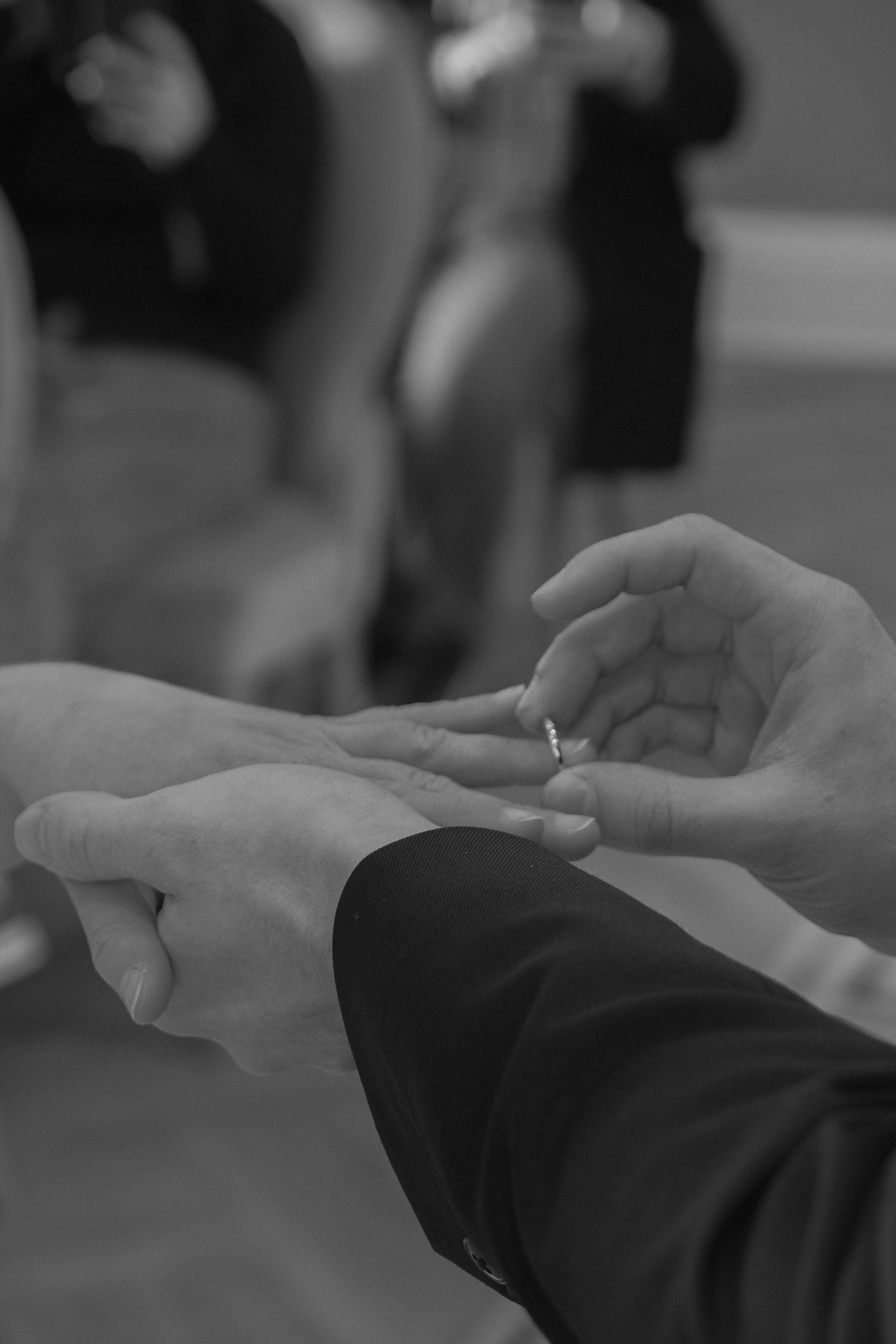 A close-up of two people exchanging rings, with one person placing a ring on the other's finger. The scene appears to be a wedding or engagement ceremony.