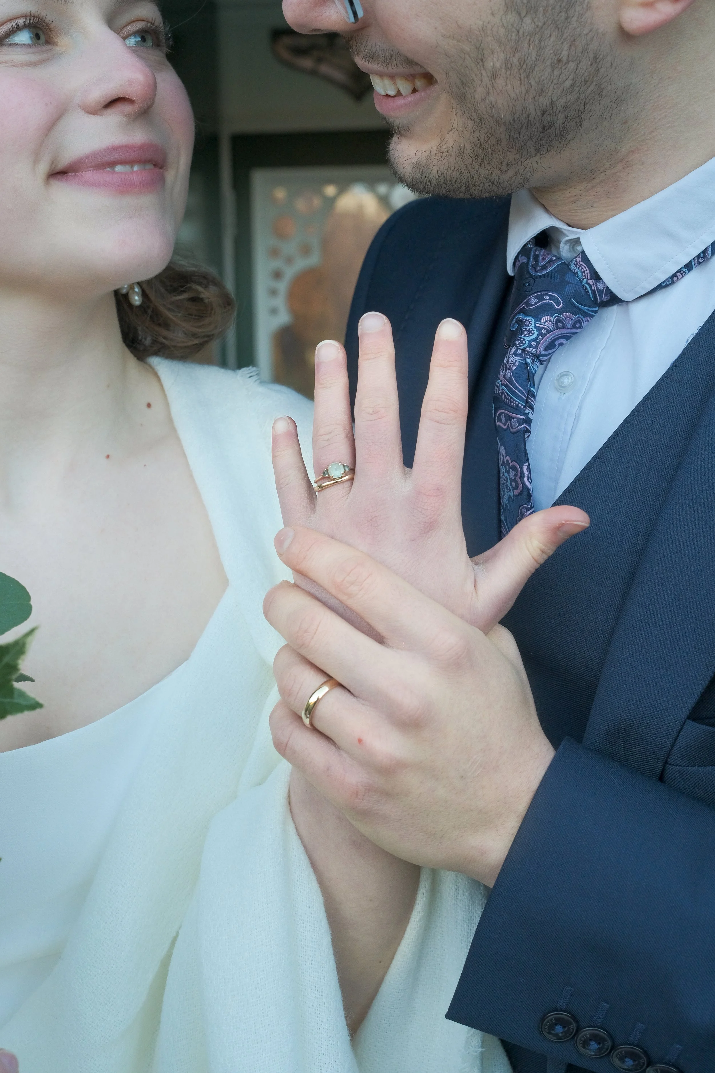 Close-up of a newly engaged couple showing off their wedding rings, smiling and gazing at each other.