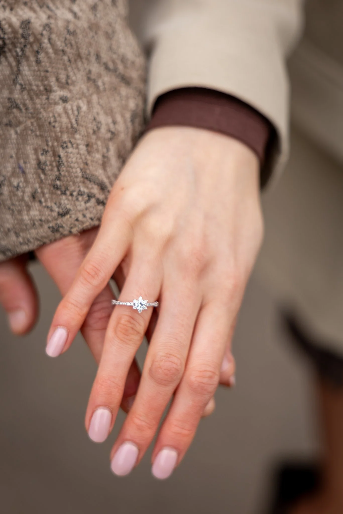 Close-up of two hands showing an engagement ring with a large gemstone on the fourth finger.