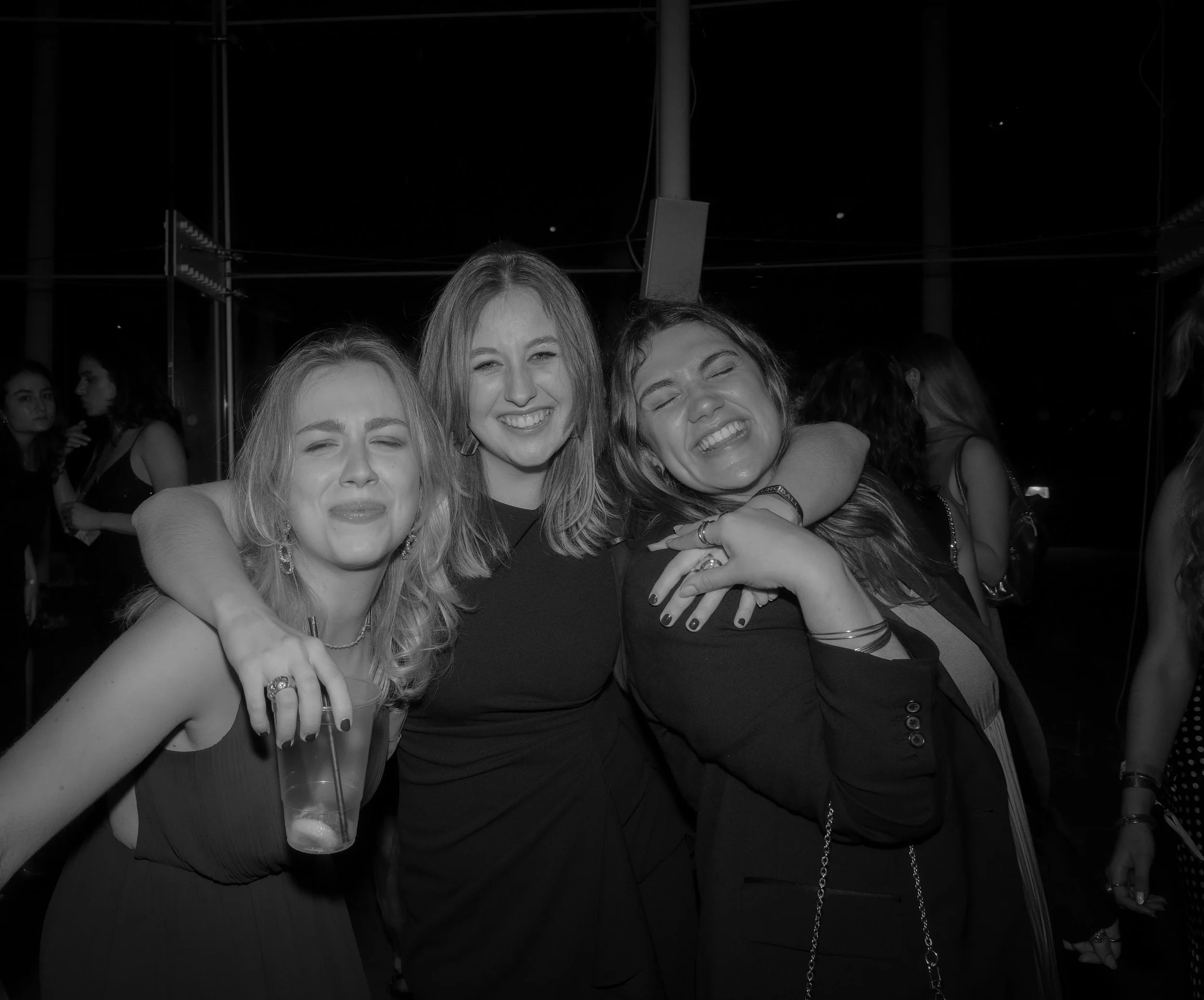 Three women smiling and hugging at a party or social gathering at night.
