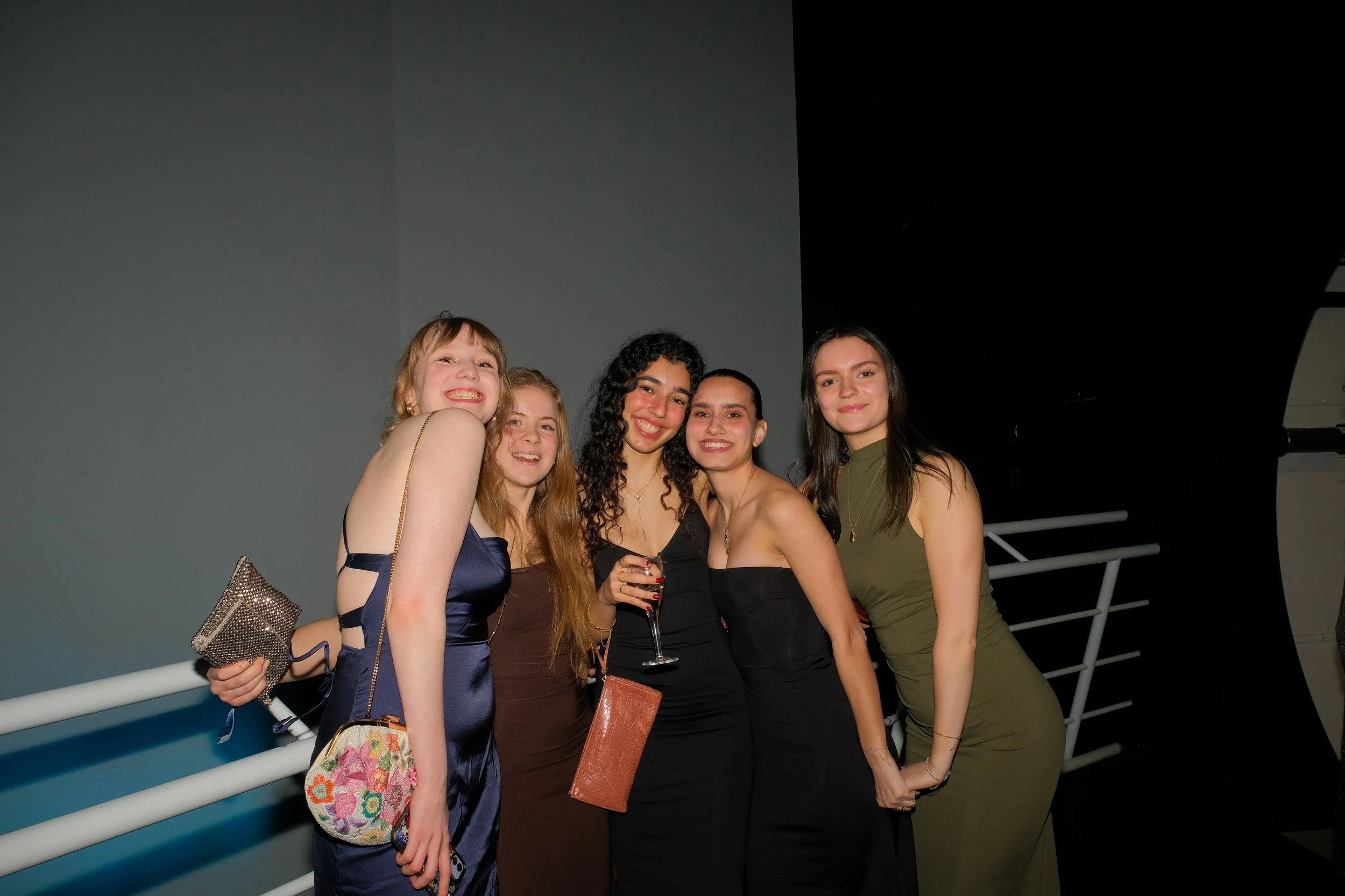 Five women in evening dresses smiling together at a social event.
