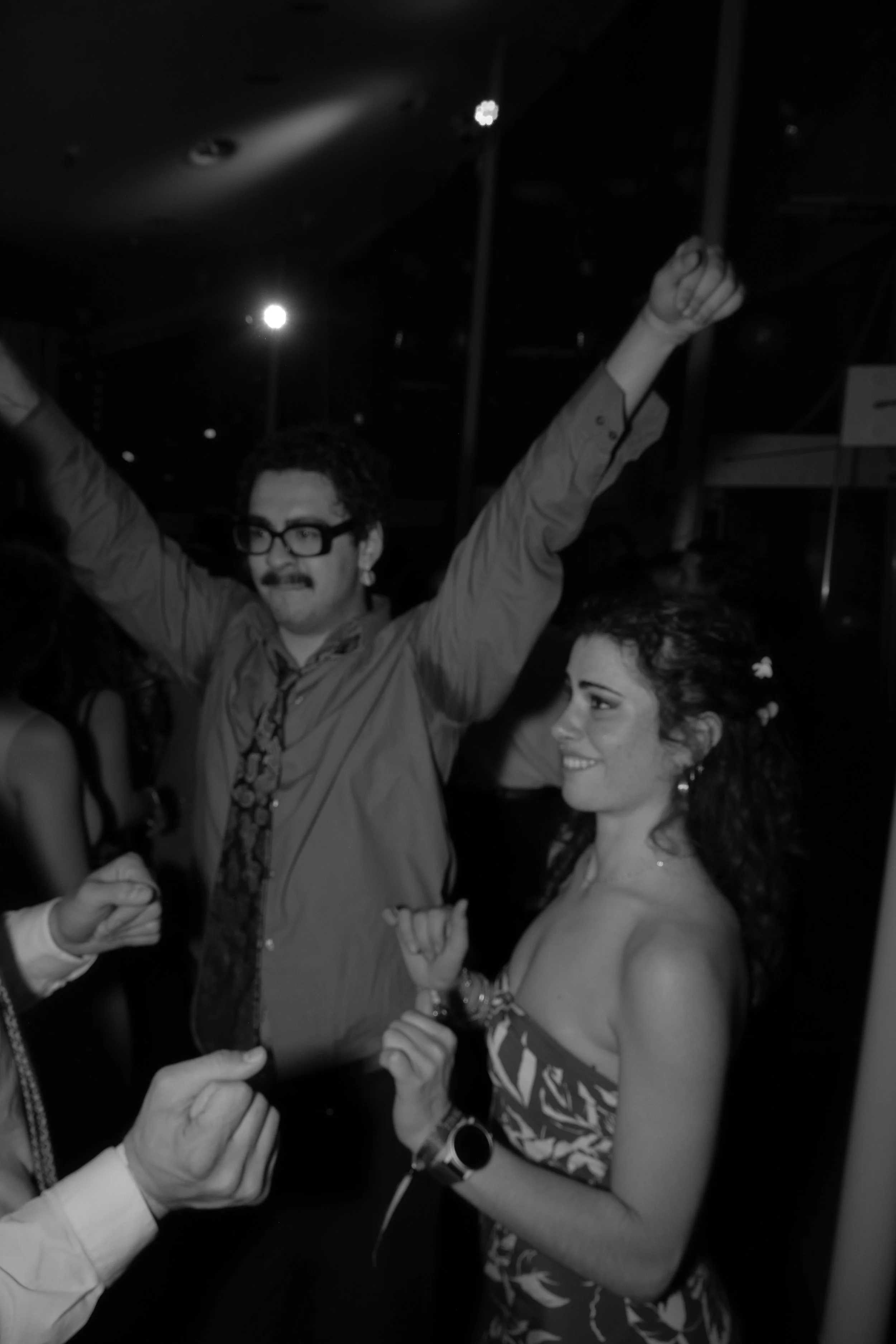 A man and woman dancing at a party, with the man raising his arms and the woman smiling.