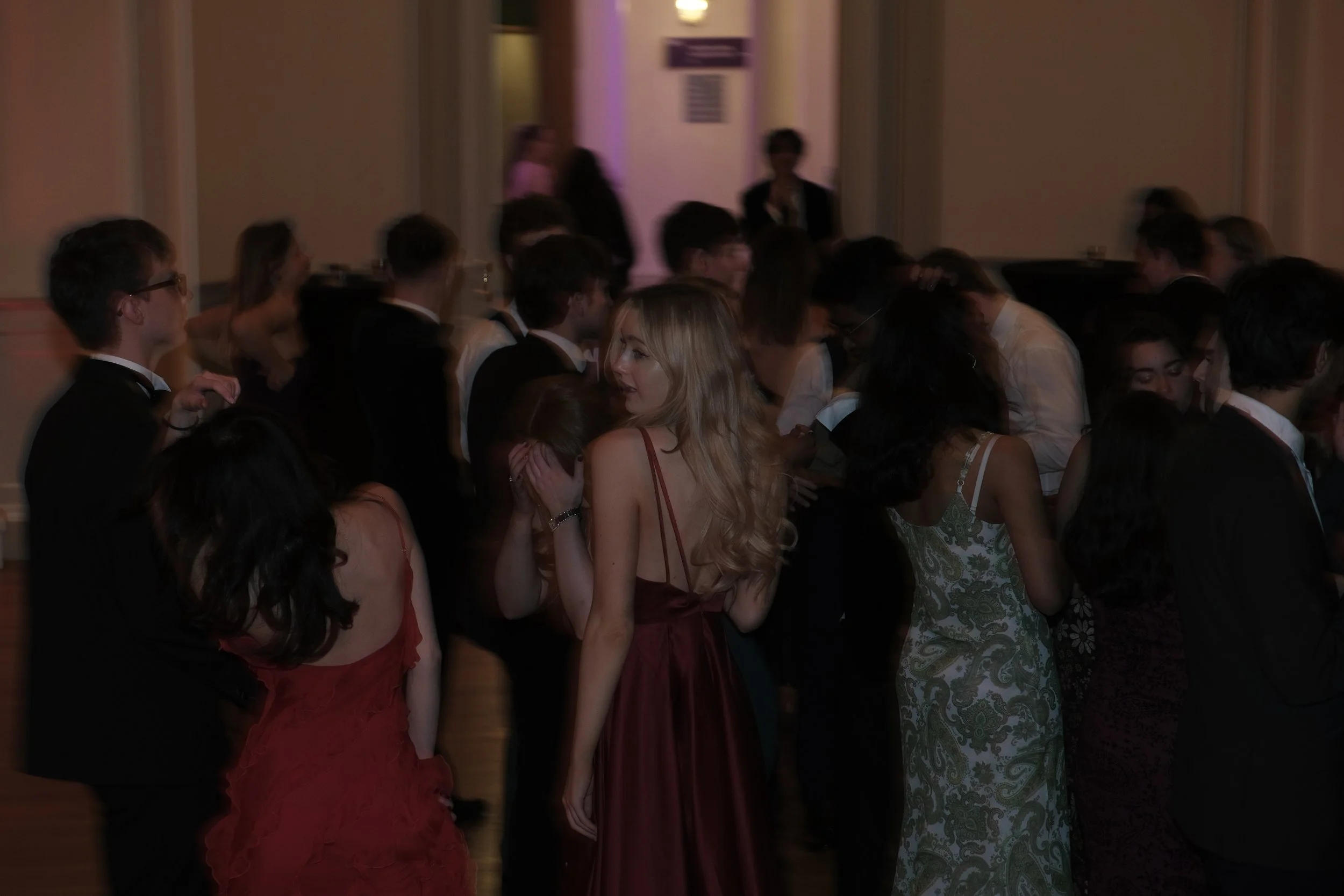 A group of people dressed in formal attire at a social event or party, standing closely together and engaged in conversation.