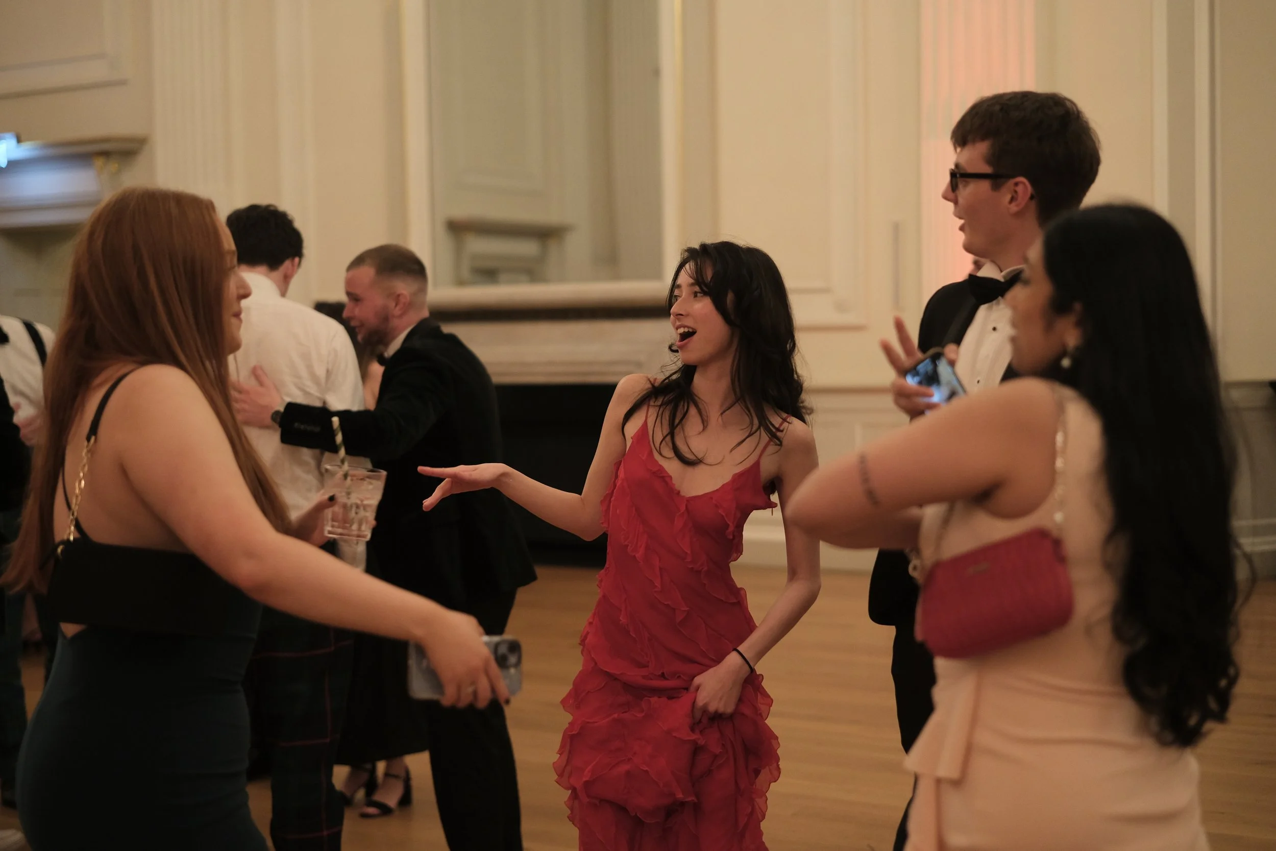 People dressed in formal attire enjoying a social event in an elegant room, engaging in conversation and laughter.