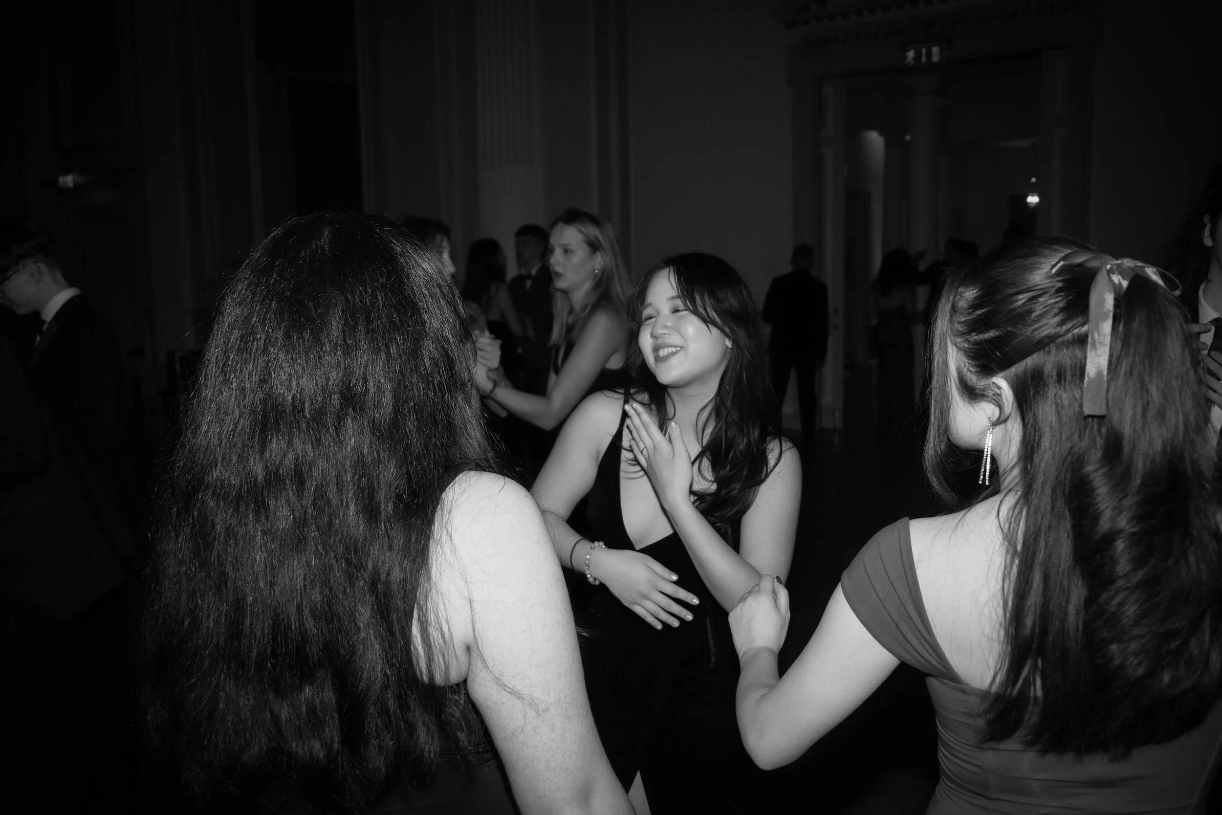 People dancing and socializing at a formal event or party, with women smiling and engaging with each other.