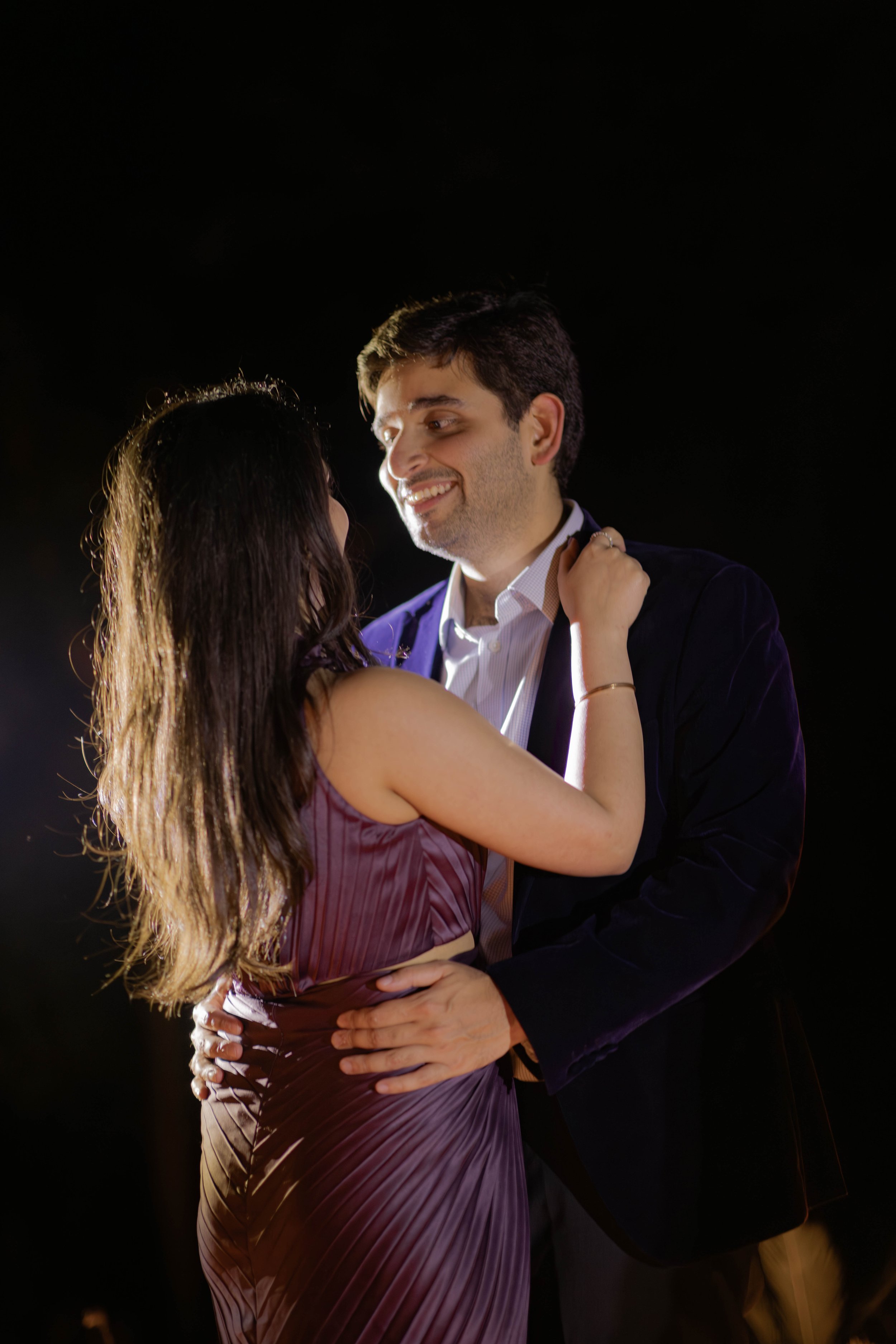 A man and woman dancing closely, smiling at each other, against a dark background.