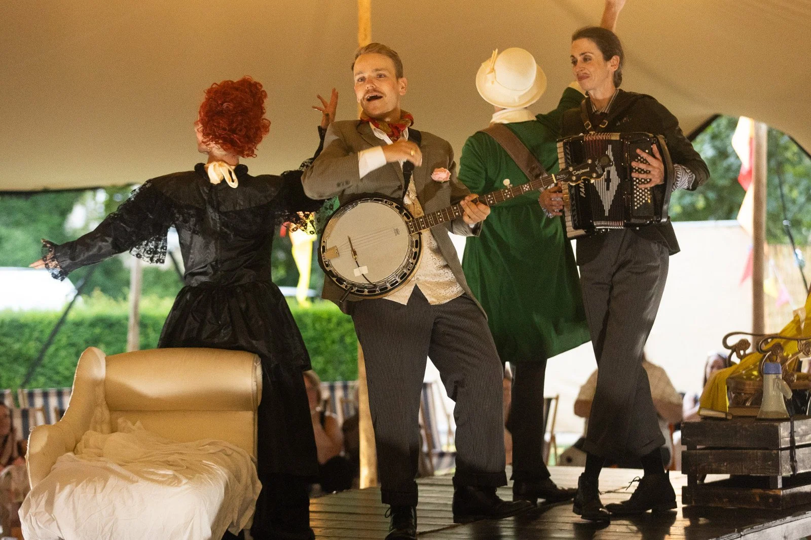 Costumed performers onstage playing a banjo and accordion in an outdoor setting.