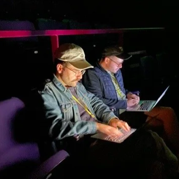 Samuel Freeman and colleague work on laptops in a dimly lit theatre.