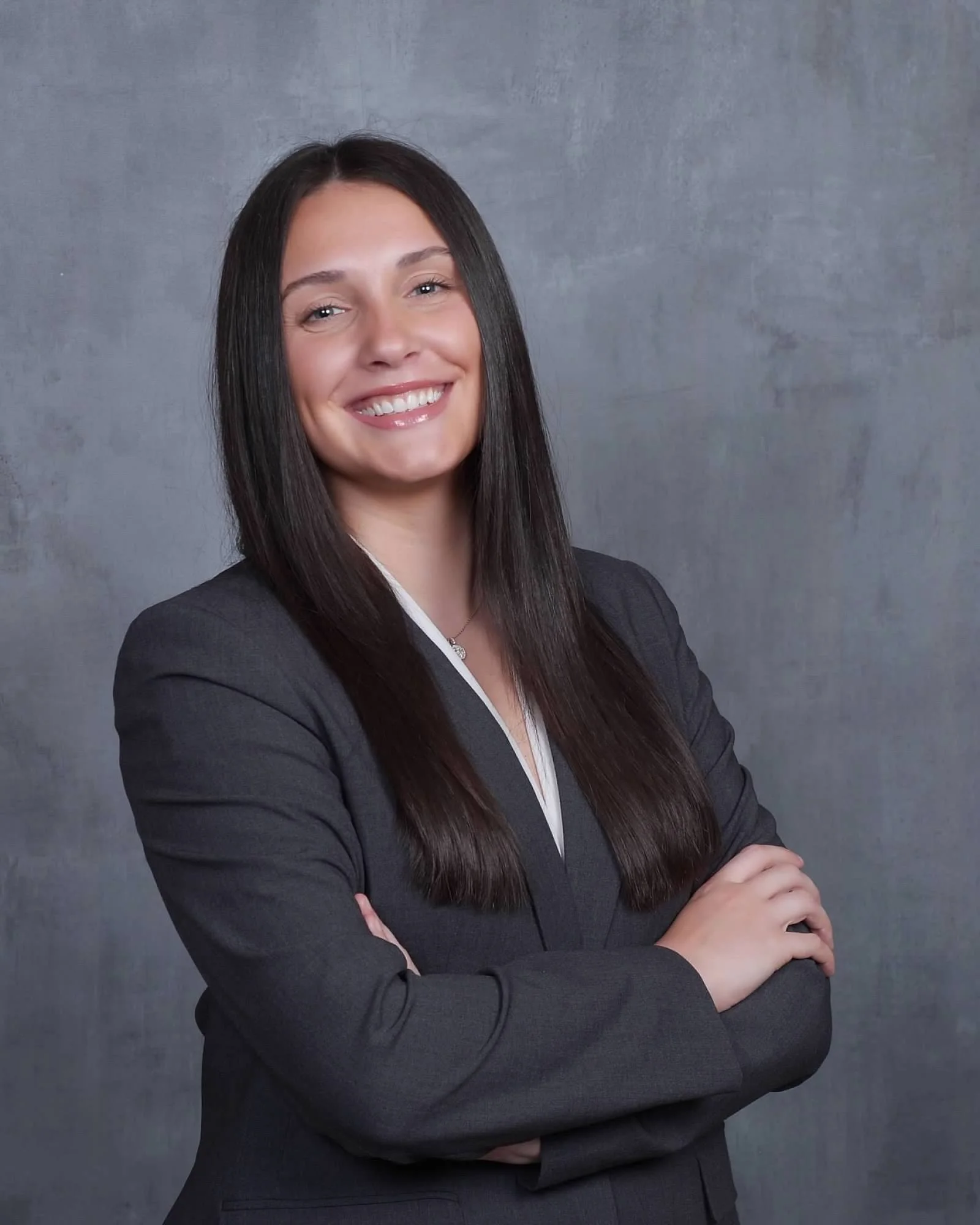 Professional woman with long dark hair smiling in a dark business suit against a gray background