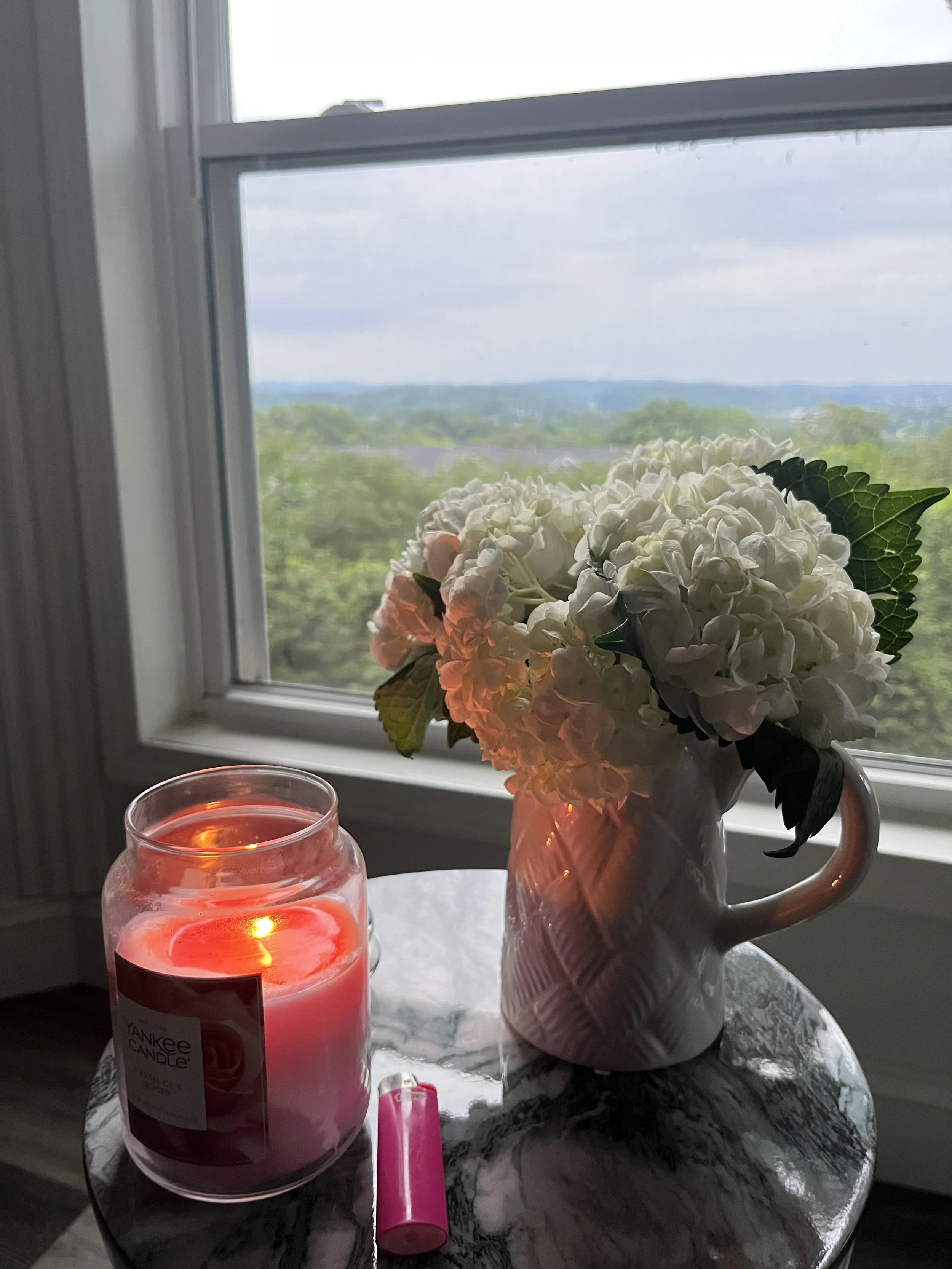 Pink candle and pastel flower arrangement in a vase on a marble table by a window