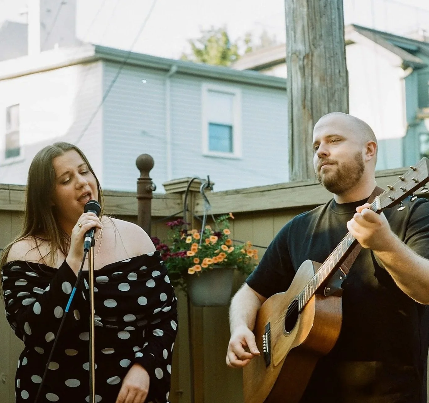 Singer performing with a microphone beside a guitarist playing acoustic guitar outdoors