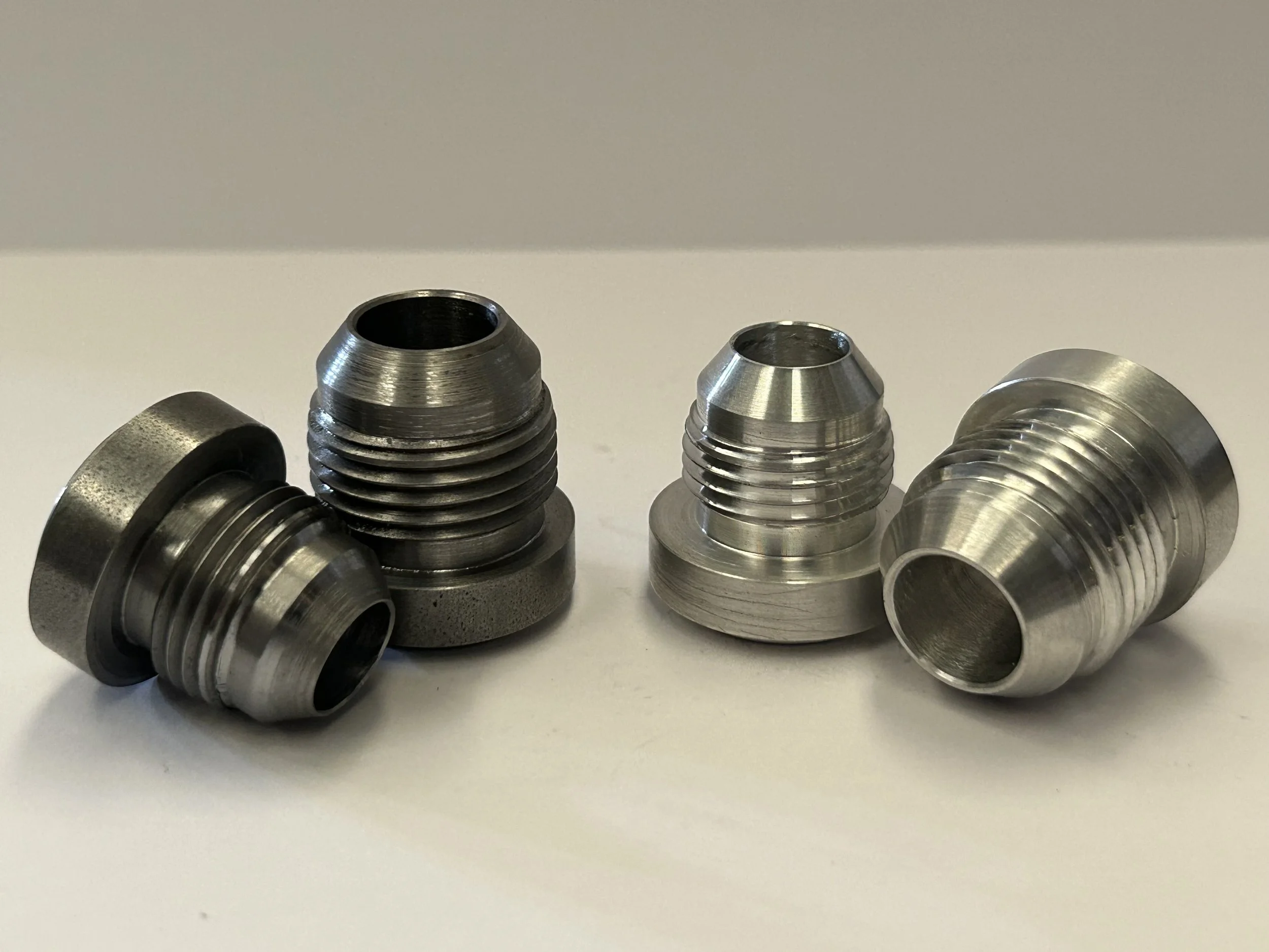 Close-up of four CNC turned AN/JIC weld-on hose fittings in steel and aluminium, highlighting precision threads, sealing cones and weld-on flanges. (Copy)