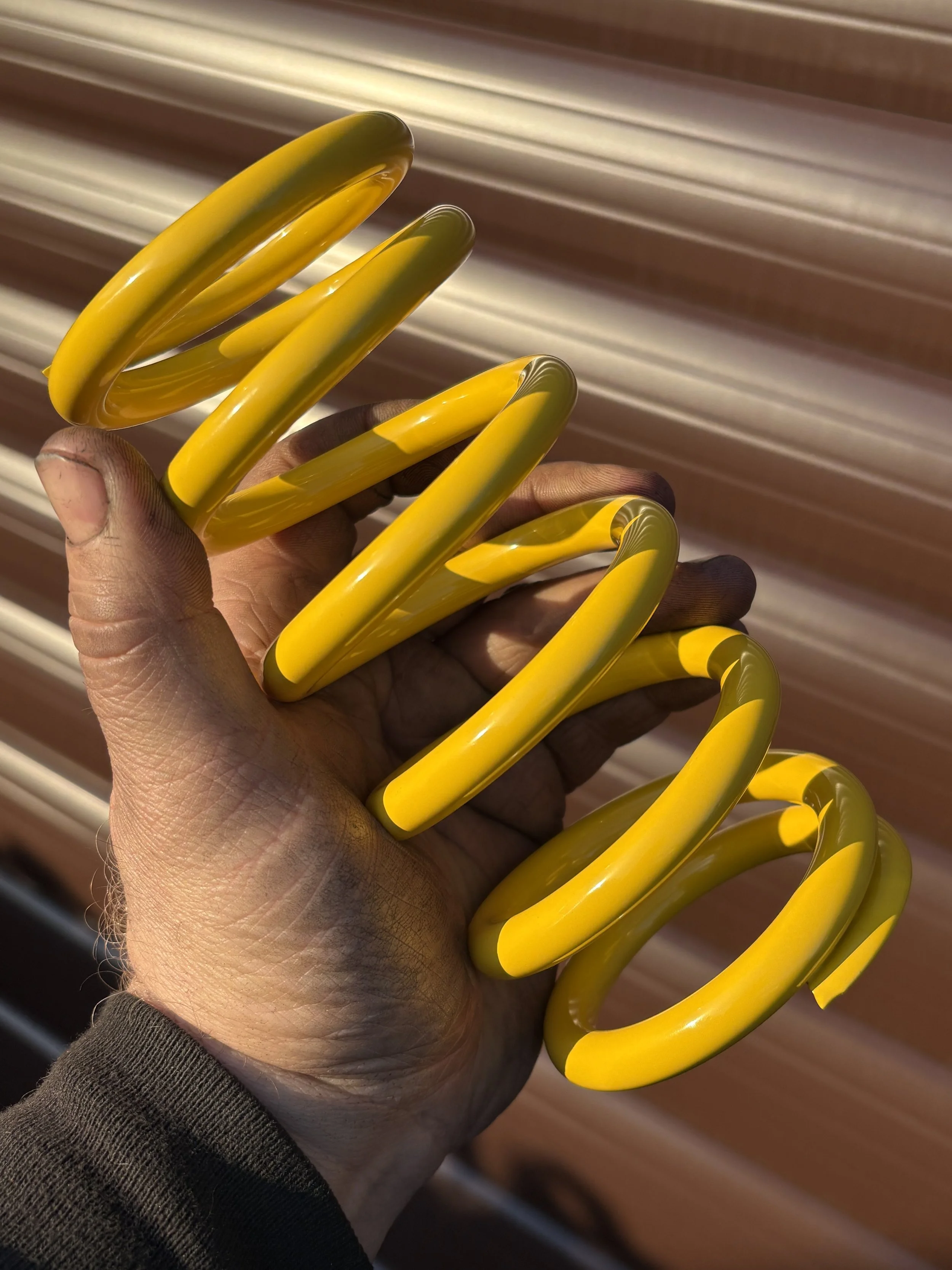 Motorcycle suspension coil spring finished in glossy yellow powder coating by PlazCutz in Morecambe, Lancashire, showing the smooth decorative finish on a customer's racing motorcycle component.