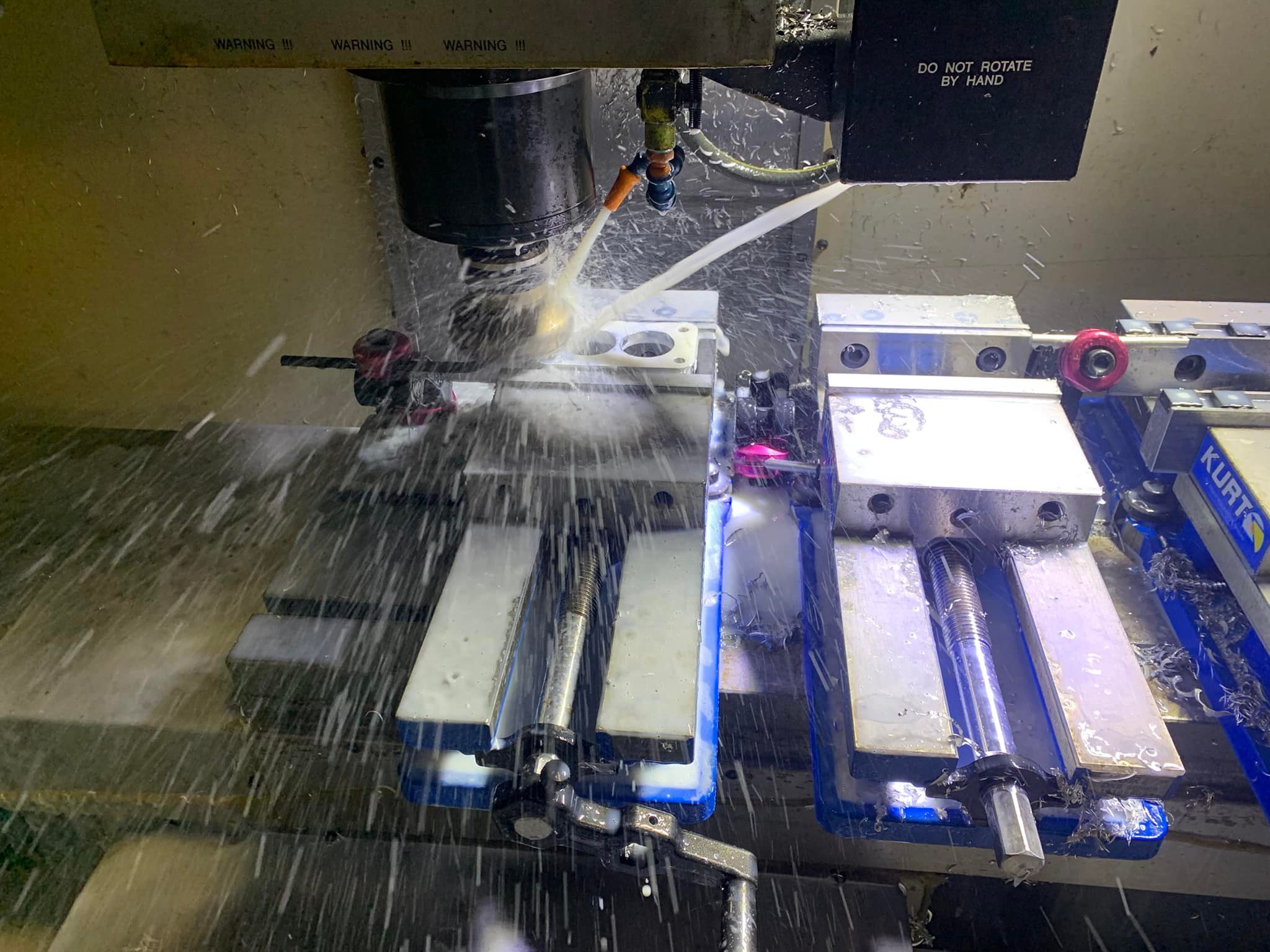 CNC milling machine cutting a metal component with coolant flowing over the workpiece inside the machining centre.