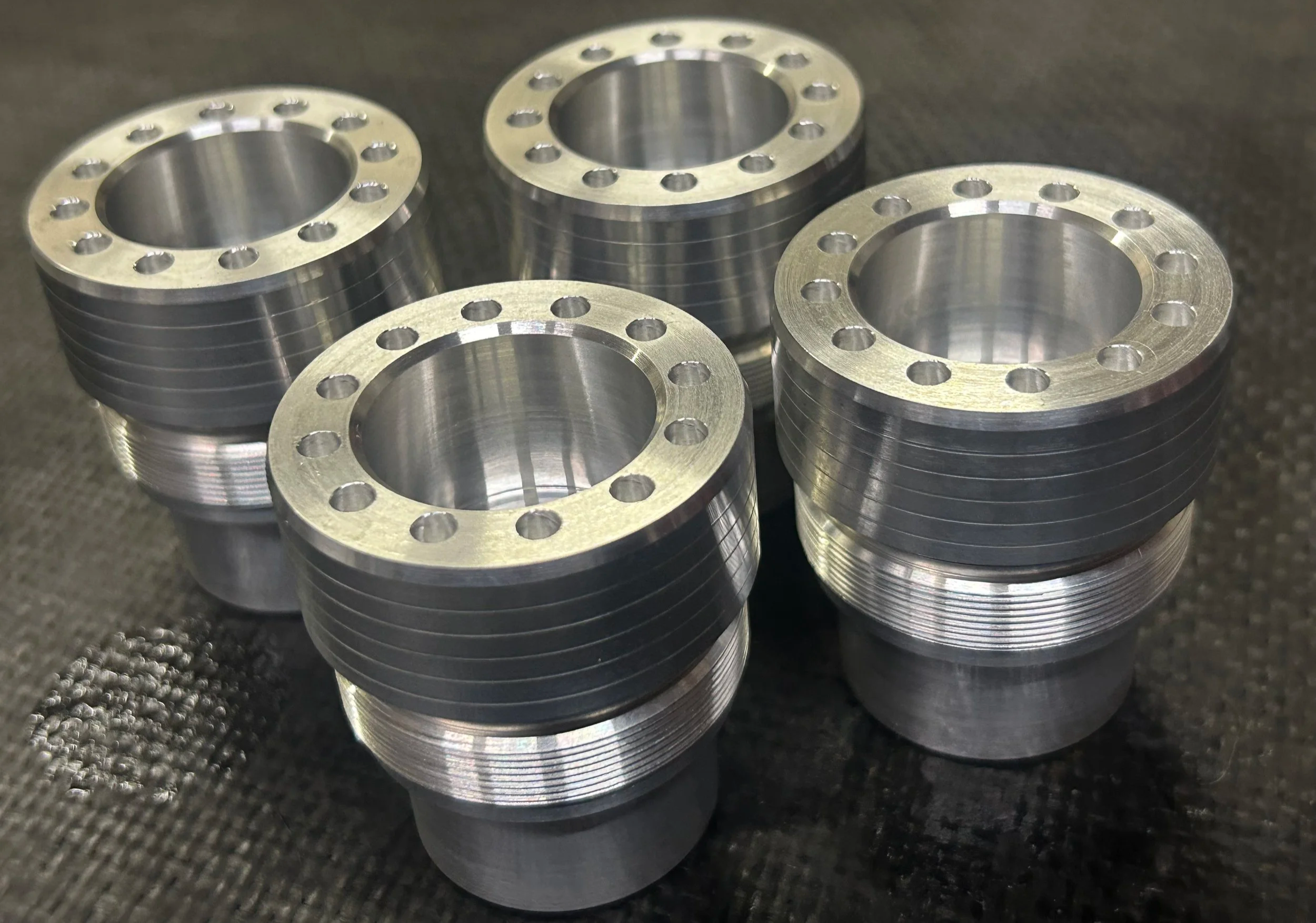 Five machined metal pipe flanges with circular bolt holes arranged on a workshop surface.