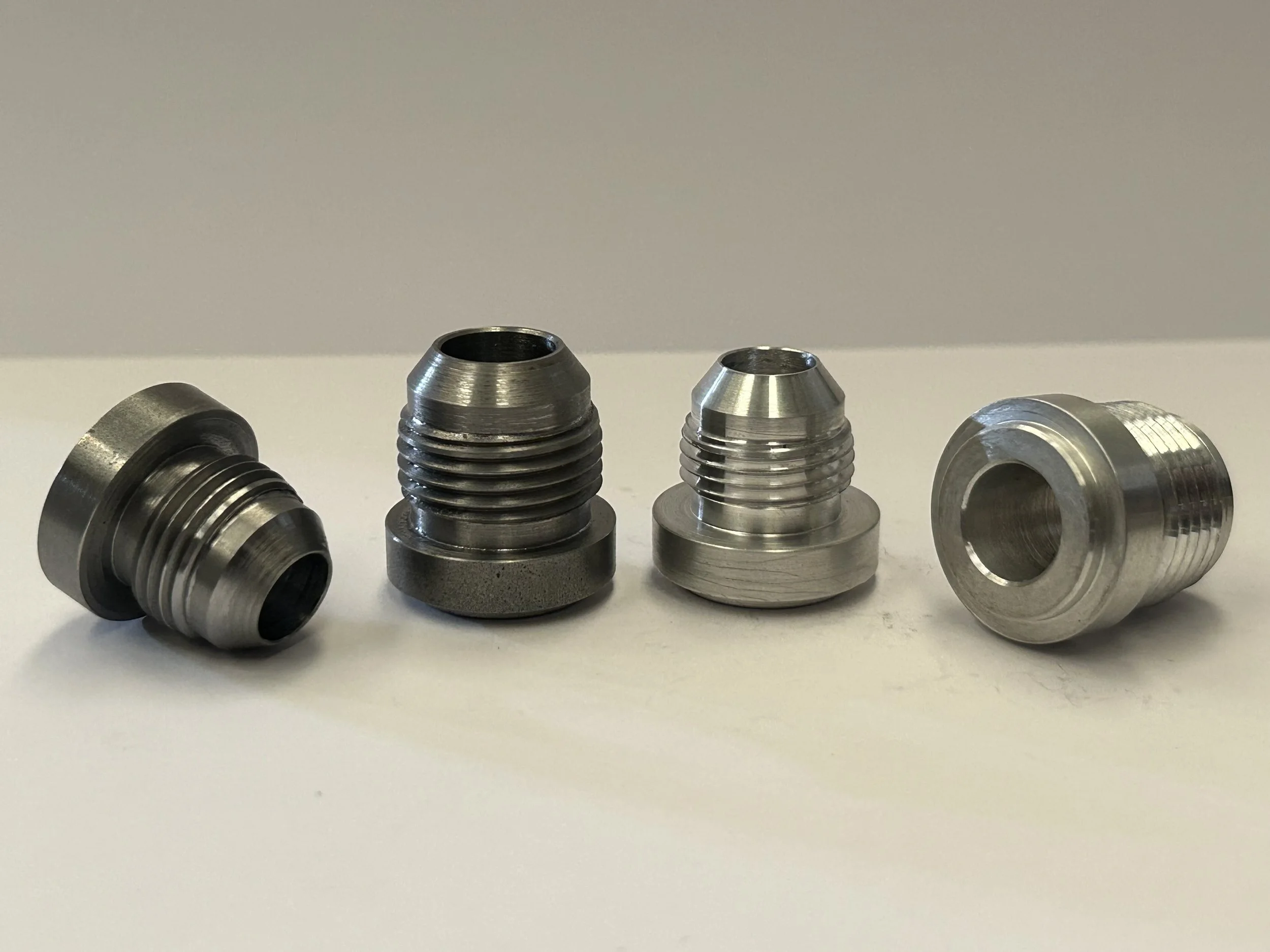 Four CNC turned AN/JIC male weld-on hose fittings in steel and aluminium, showing different sizes, threaded connections and machined flanges. (Copy)