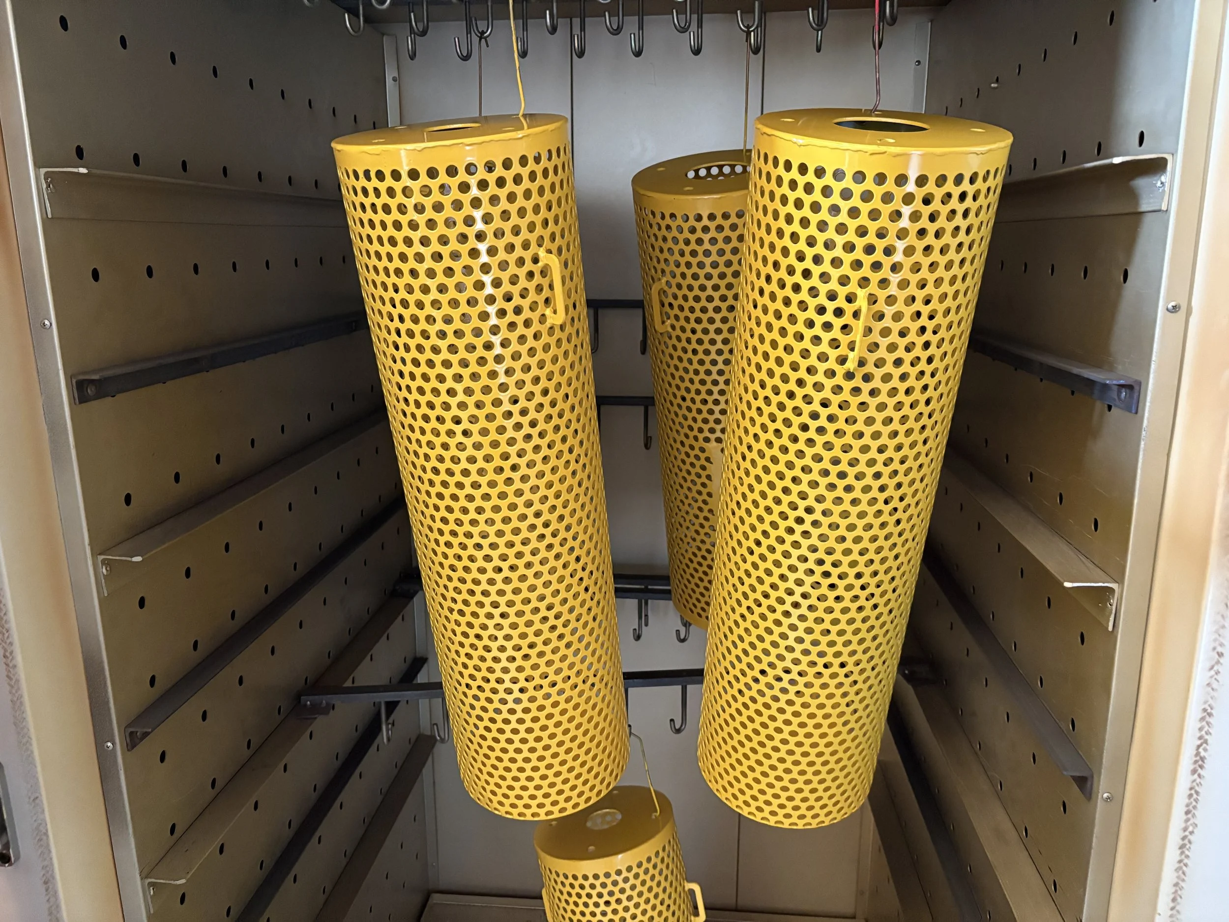 Bright yellow powder-coated perforated steel components hanging inside the PlazCutz curing oven, demonstrating our in-house powder coating facilities.
