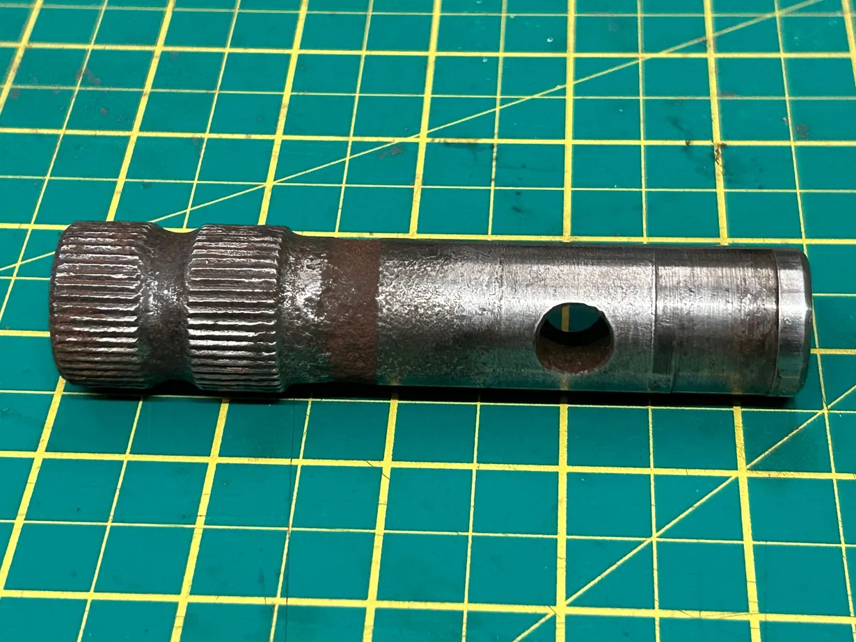Worn steel shaft with splined section and cross-drilled hole before engineering repair at PlazCutz in Lancashire.