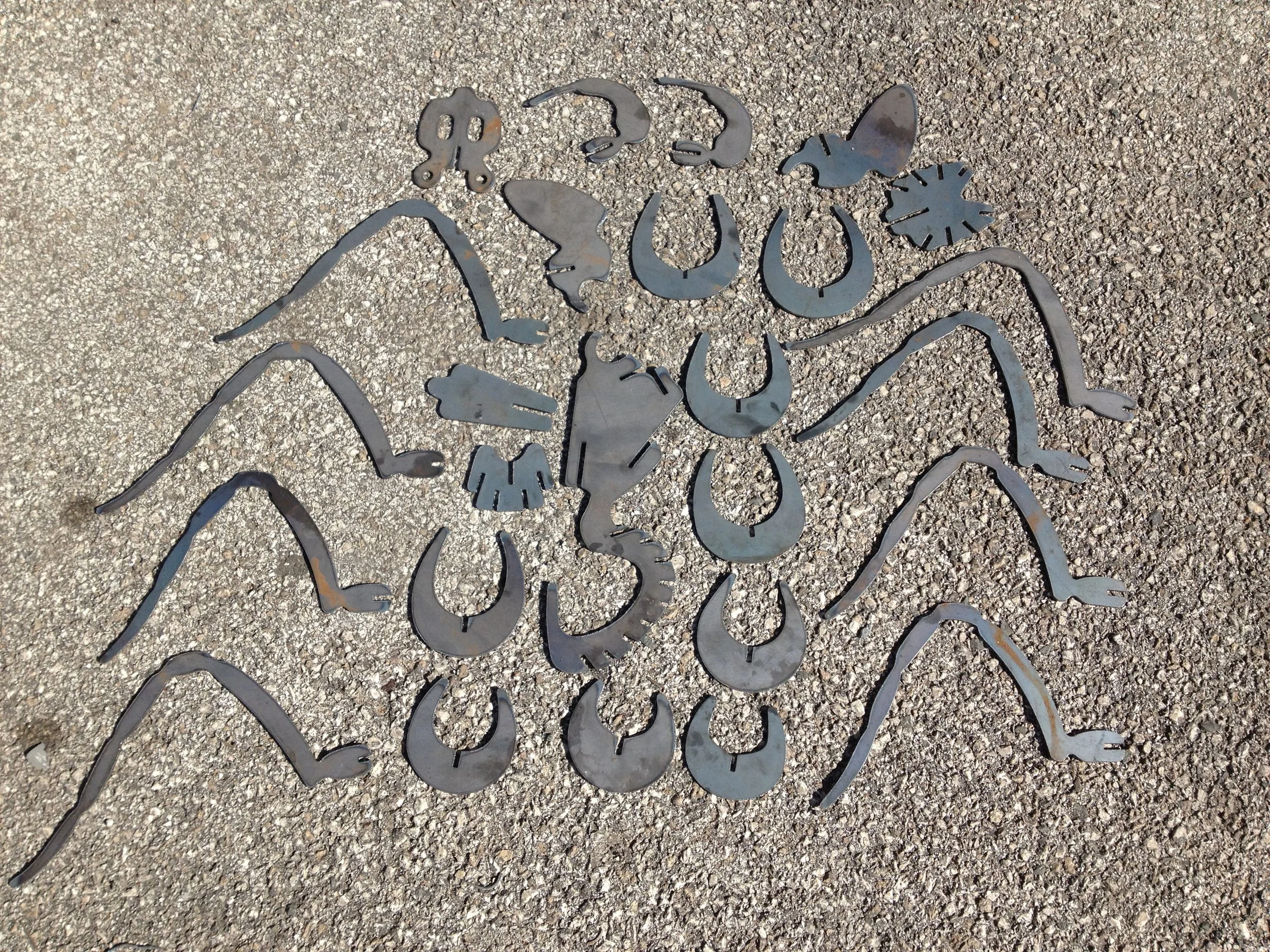 CNC plasma-cut steel spider components laid out before assembly, showing eight curved legs, slotted body sections and connecting pieces manufactured from the Spider 3D DXF design.