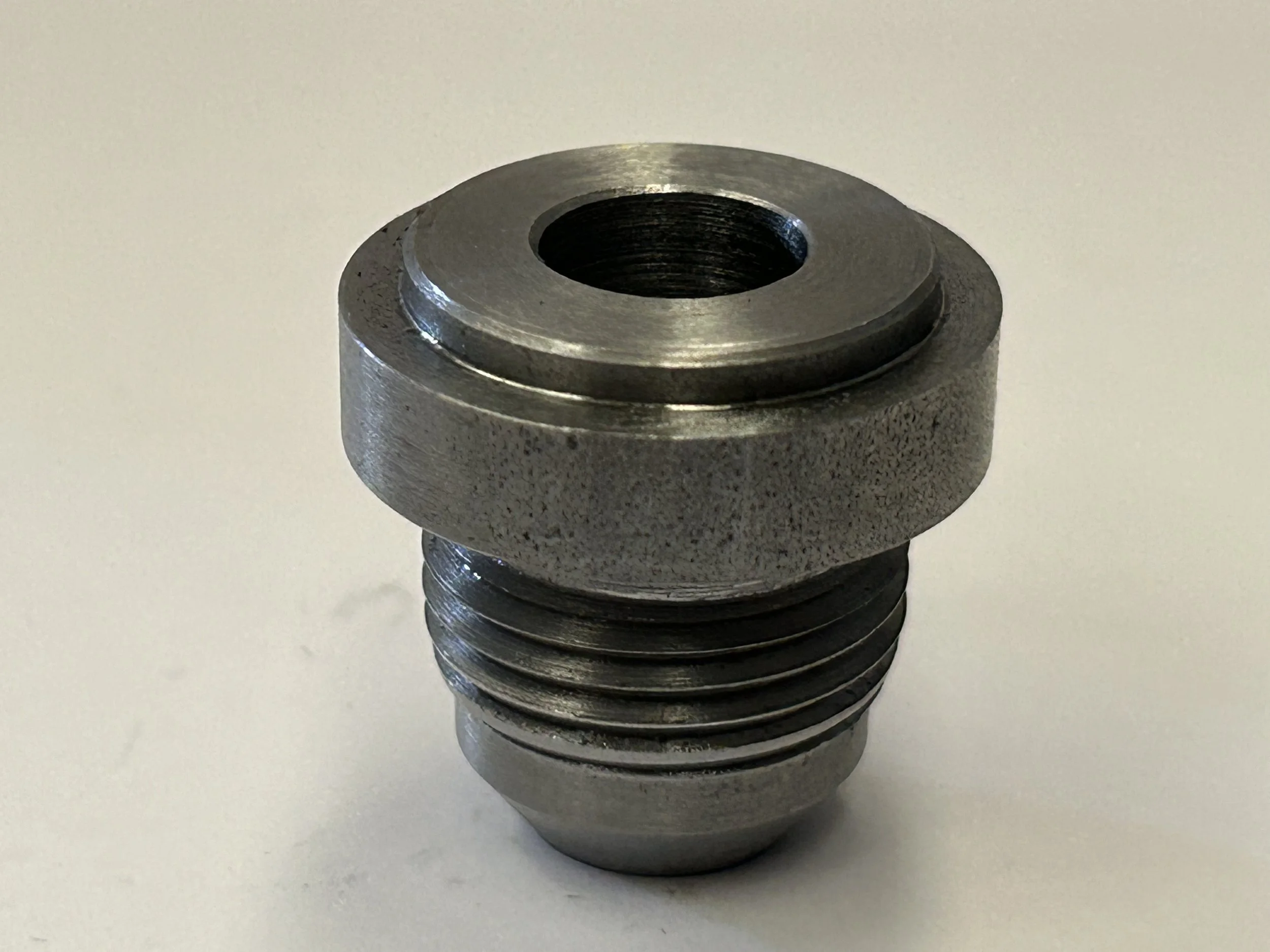 CNC turned AN-10 JIC male weld-on hose fitting in EN8 steel, showing the machined flange, central bore and threaded connection from above.