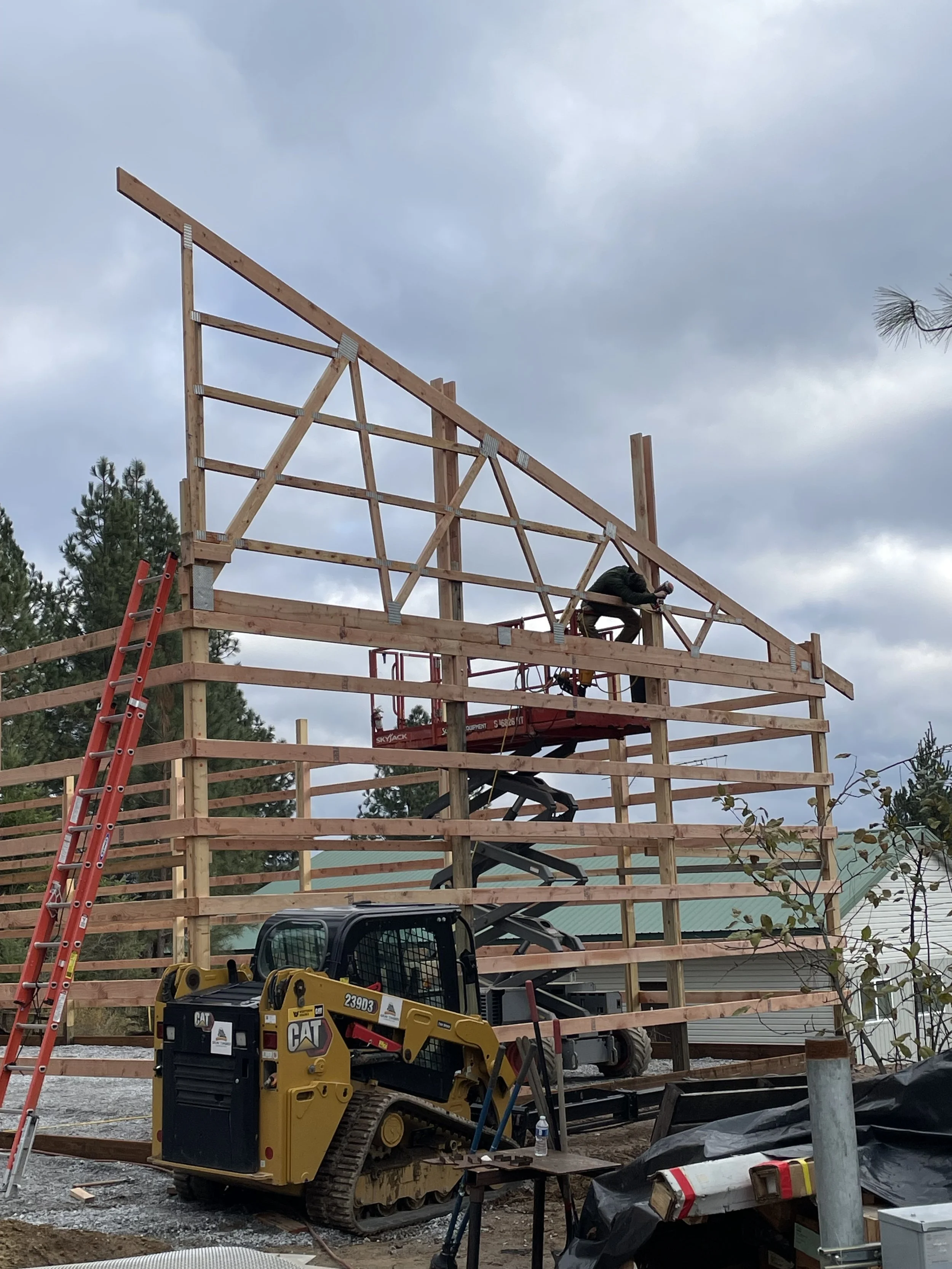 Construction worker framing a wooden building beside a red ladder and CAT compact track loader