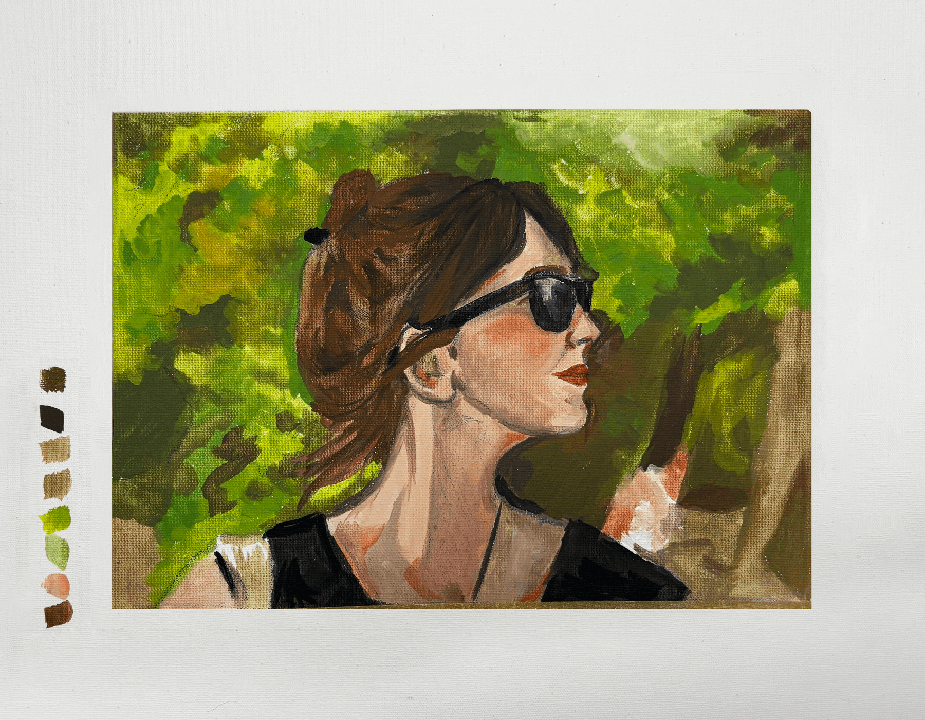 Retrato de uma mulher com cabelo castanho, usando óculos escuros, camiseta preta e brincos, ao ar livre com árvores verdes ao fundo.