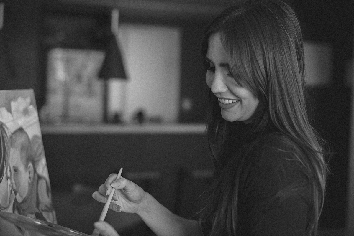 Mulher sorrindo enquanto pinta um quadro em um ambiente interno.