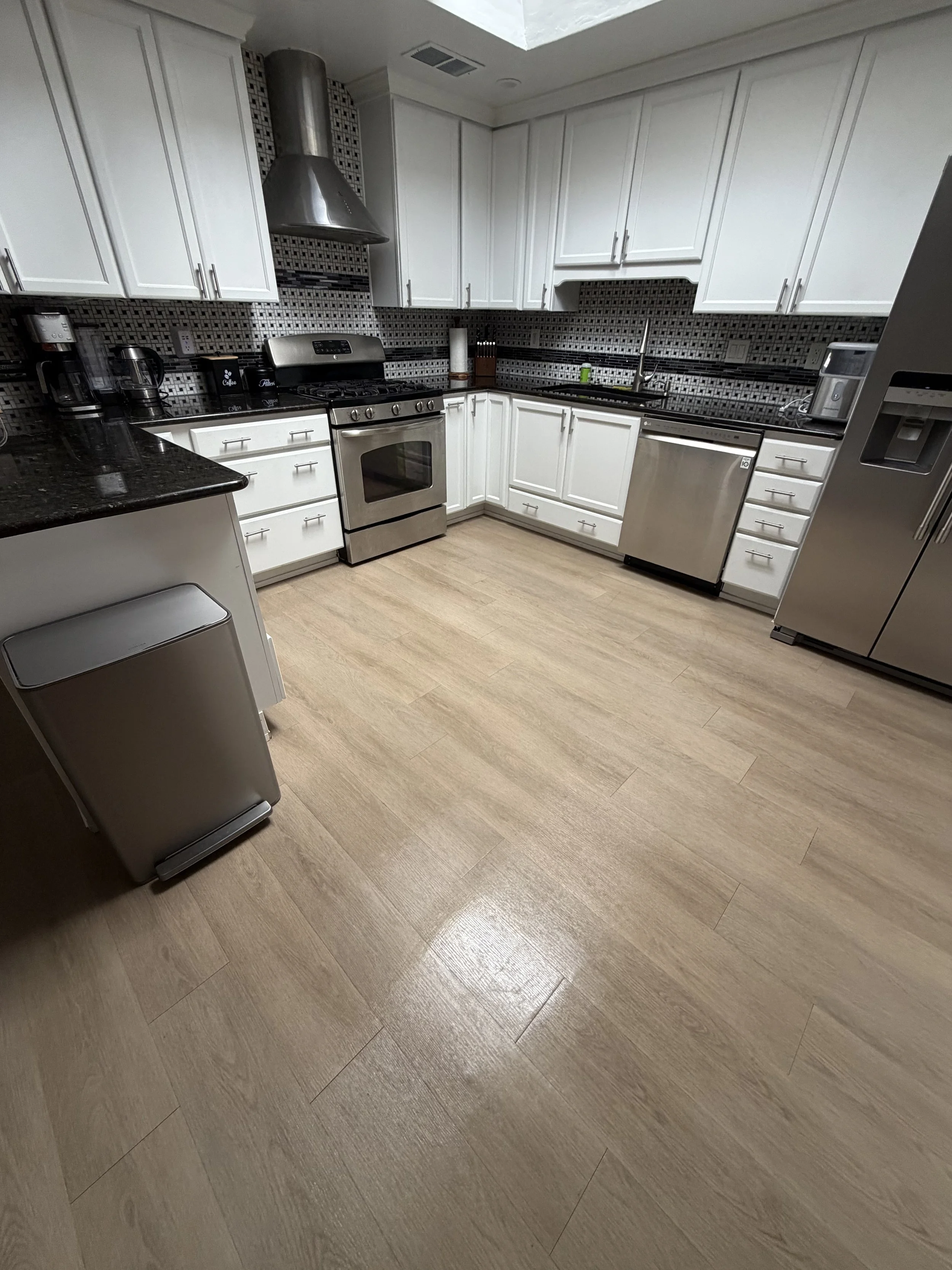 Modern kitchen with white cabinets, black mosaic tile backsplash, stainless steel range, dishwasher, refrigerator, and dark granite countertops.