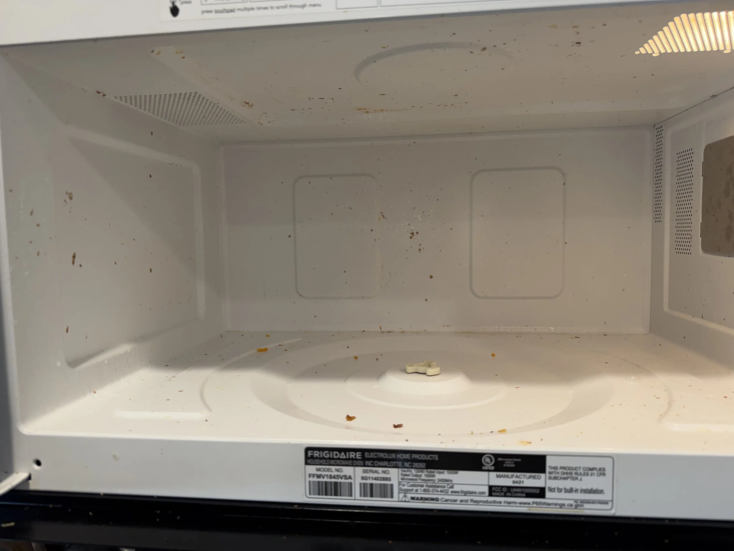 Dirty, empty Frigidaire microwave interior with food crumbs and stains on the walls and turntable.