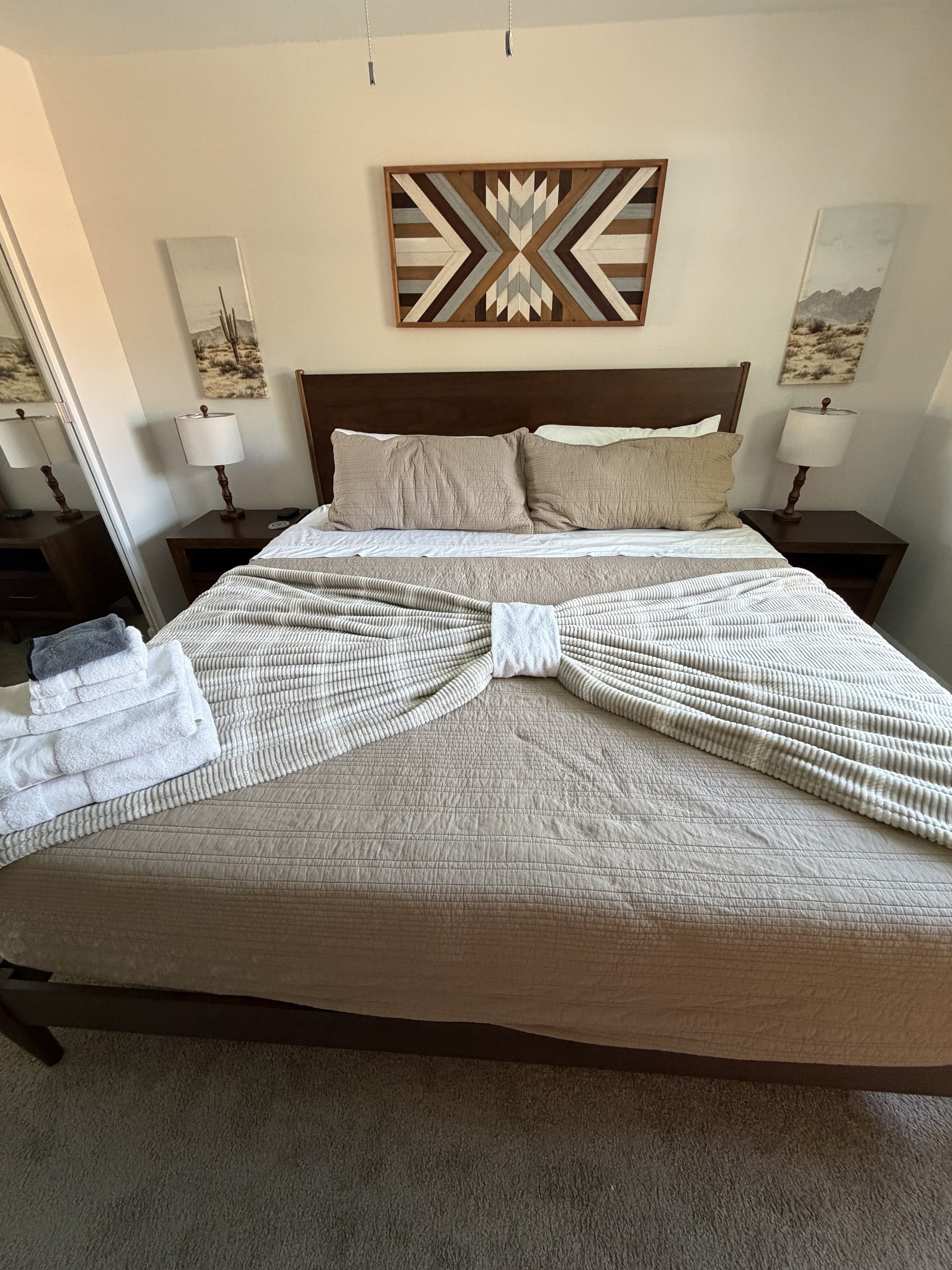 Cozy bedroom with a neatly made bed, geometric wall art, matching bedside lamps, and desert landscape prints.