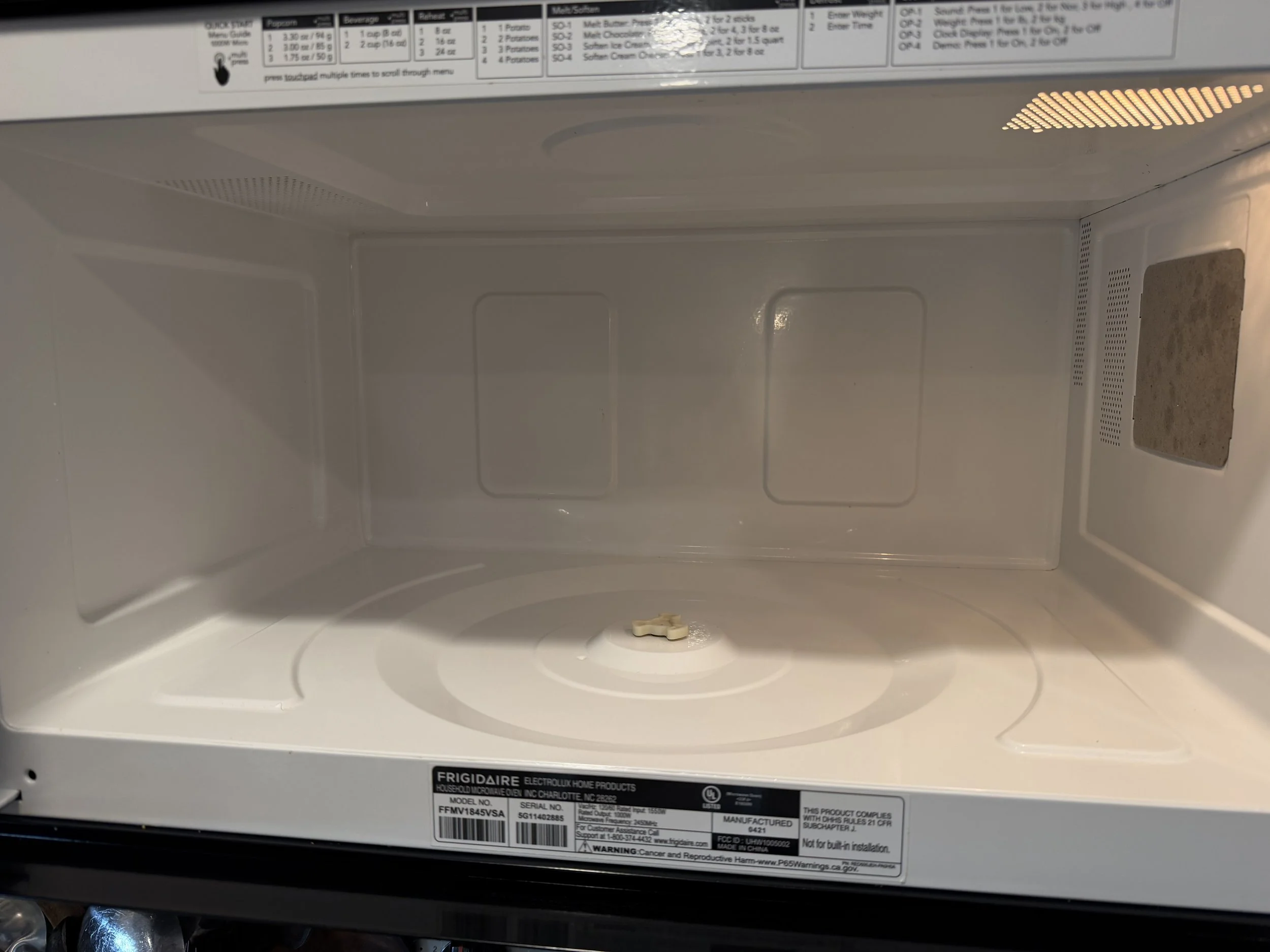 Empty Frigidaire countertop microwave interior with glass turntable, cooking guide, and side ventilation filter