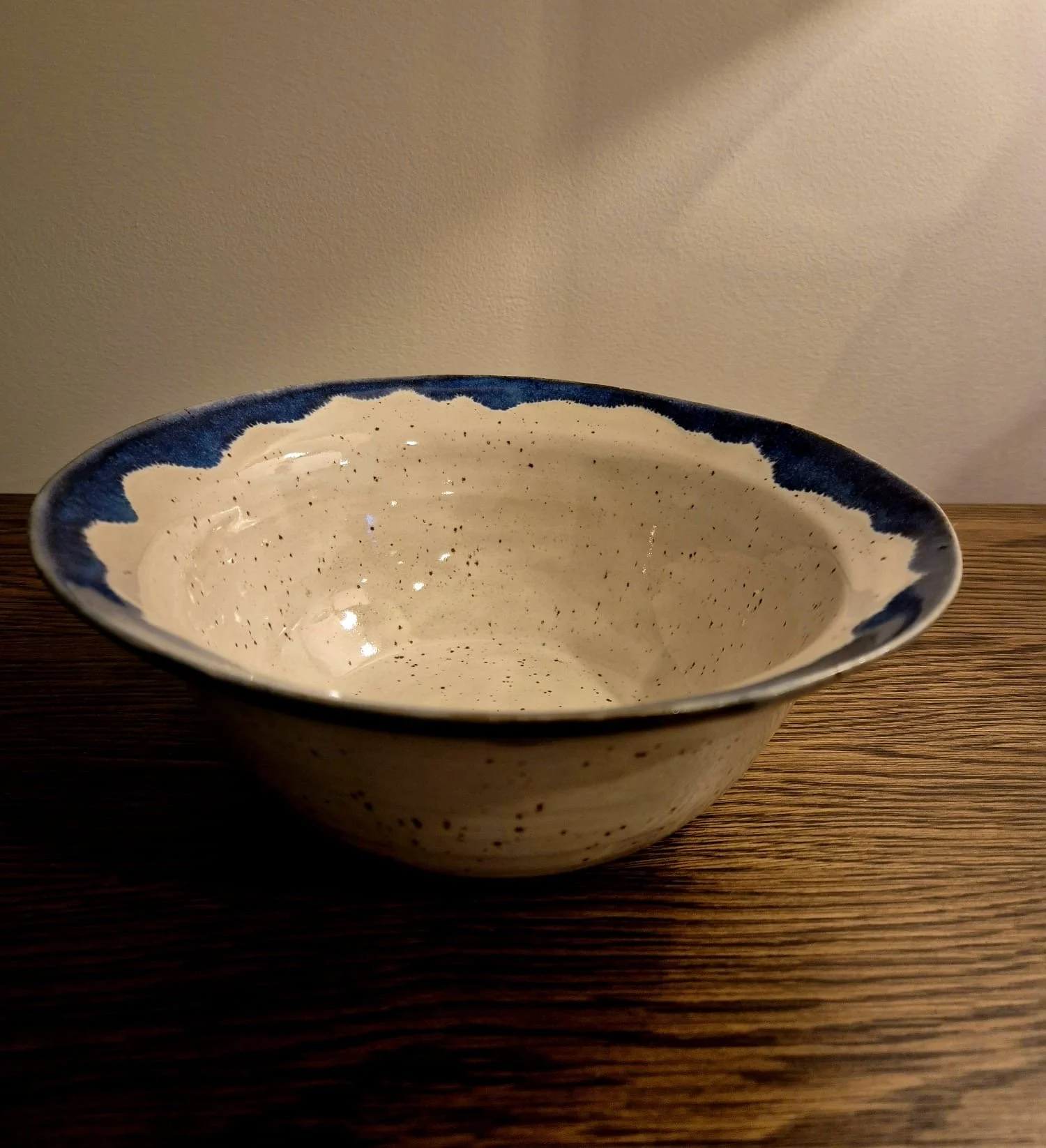 Empty speckled ceramic serving bowl with a dark blue rim on a wooden table