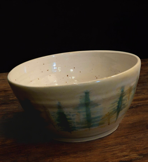 Handcrafted ceramic bowl with cream glaze and blue-green abstract brushstrokes on a wooden table