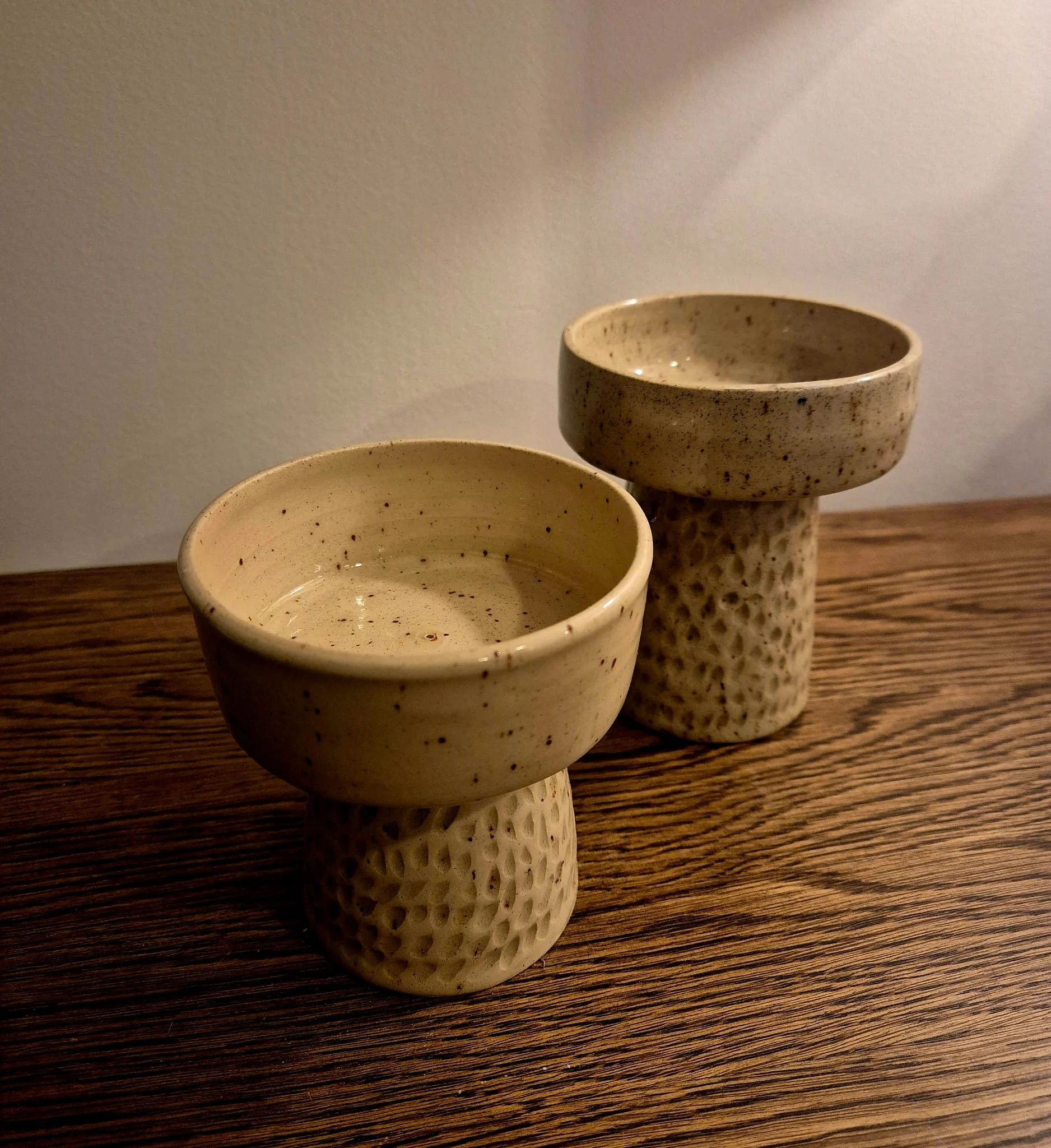 Three handmade speckled ceramic bowls and cups on a wooden table