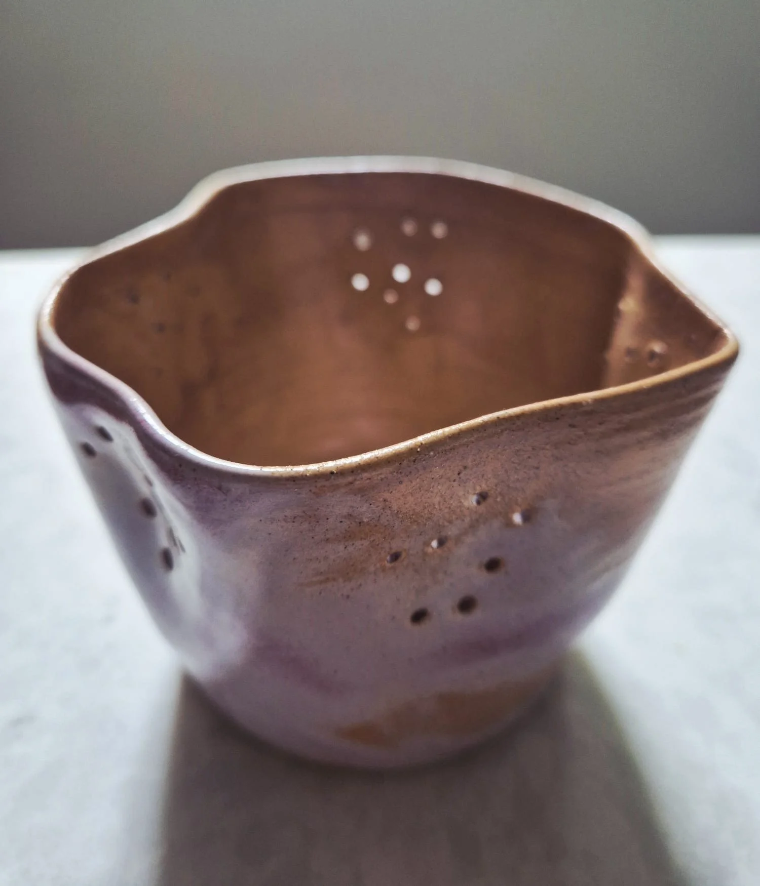 Handcrafted brown ceramic bowl with a cream rim and decorative perforations