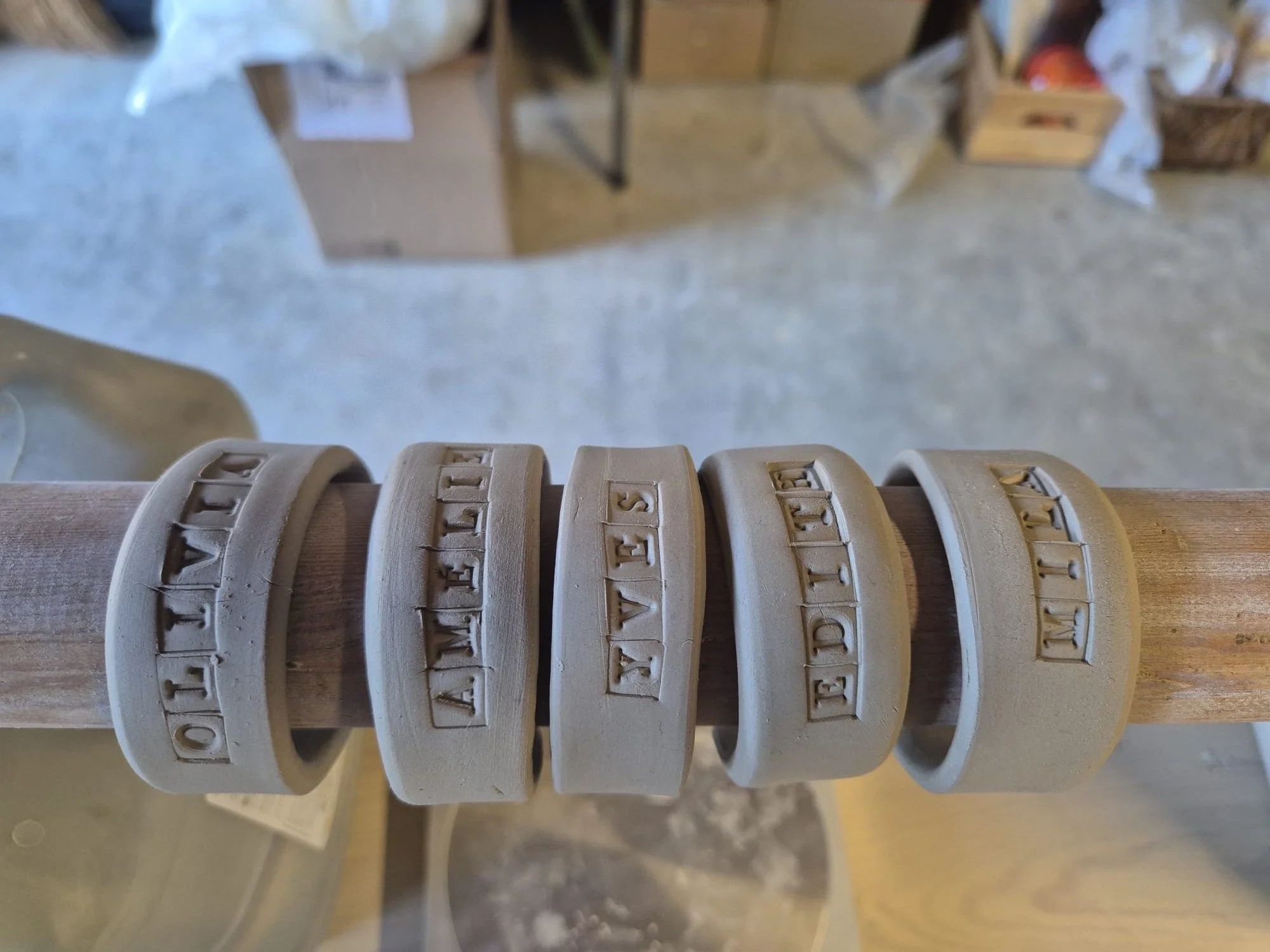 Five clay-textured bands with raised lettering displayed on a wooden rod.