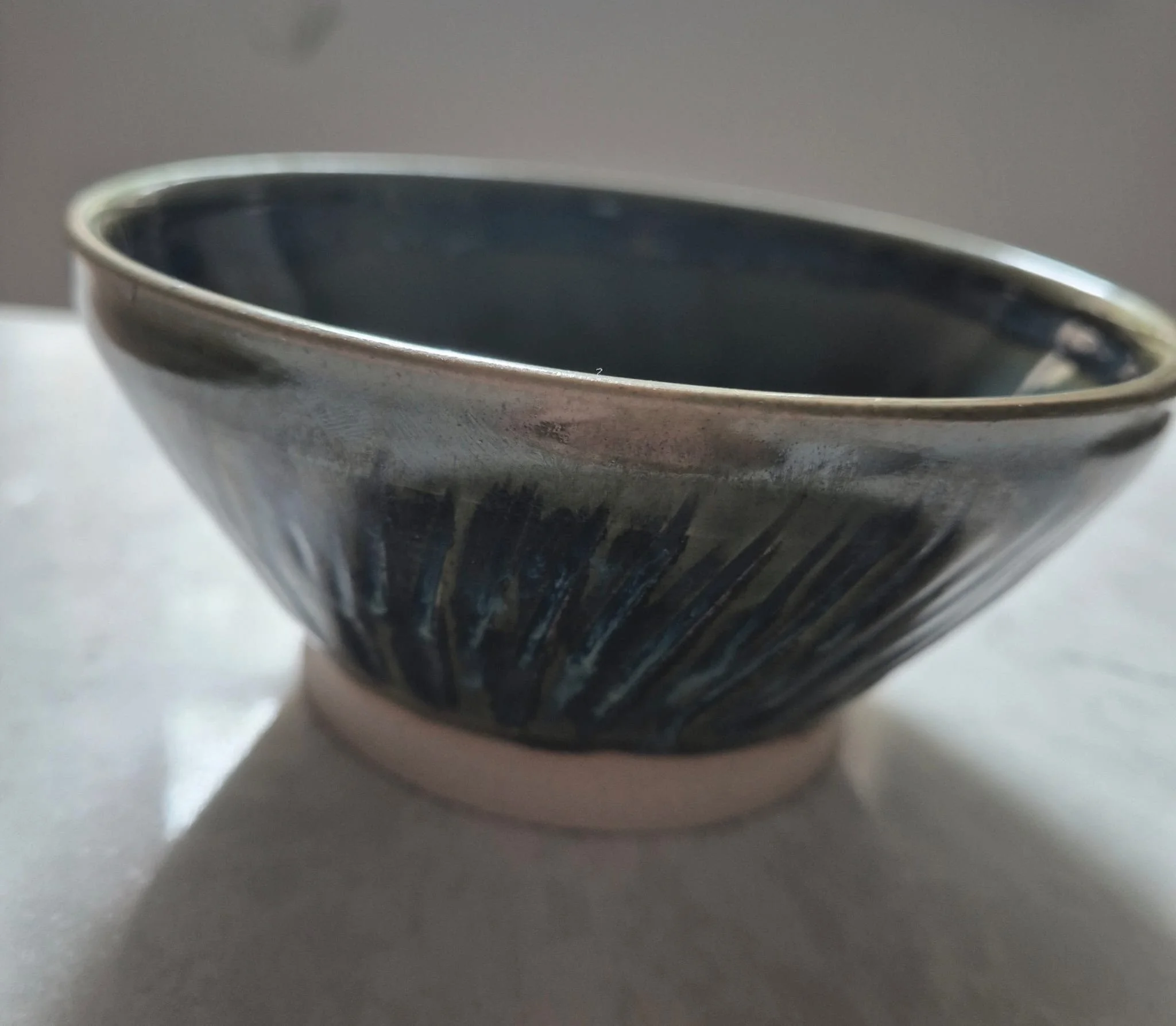 Close-up of a dark glazed ceramic bowl with a metallic rim and textured radial pattern