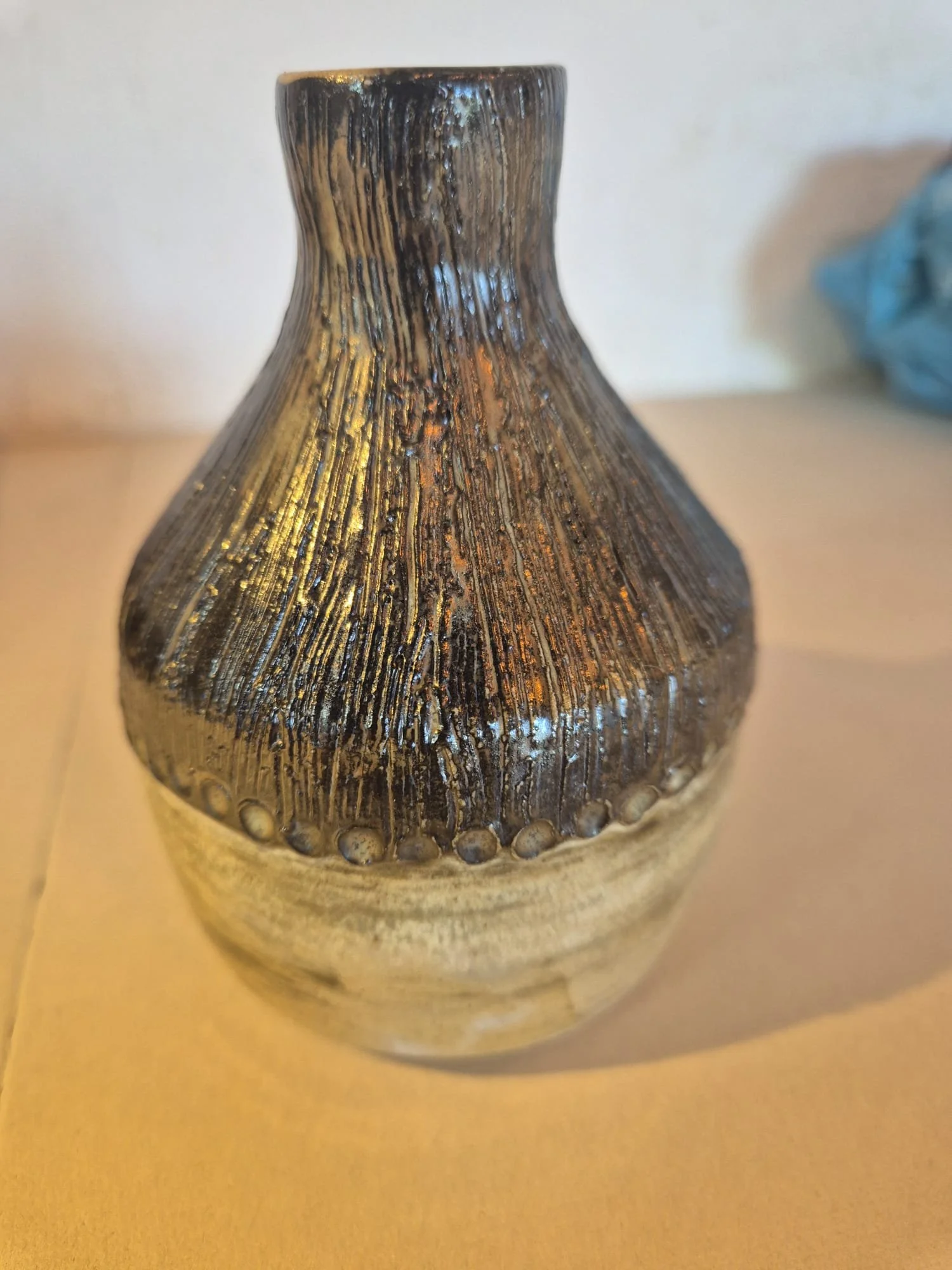 Close-up of a dark brown, vertically textured ceramic vase with a rounded base and narrow neck on a wooden table