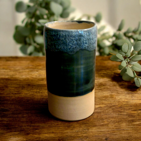 Handcrafted blue and cream ceramic tumbler on a wooden table, surrounded by eucalyptus branches