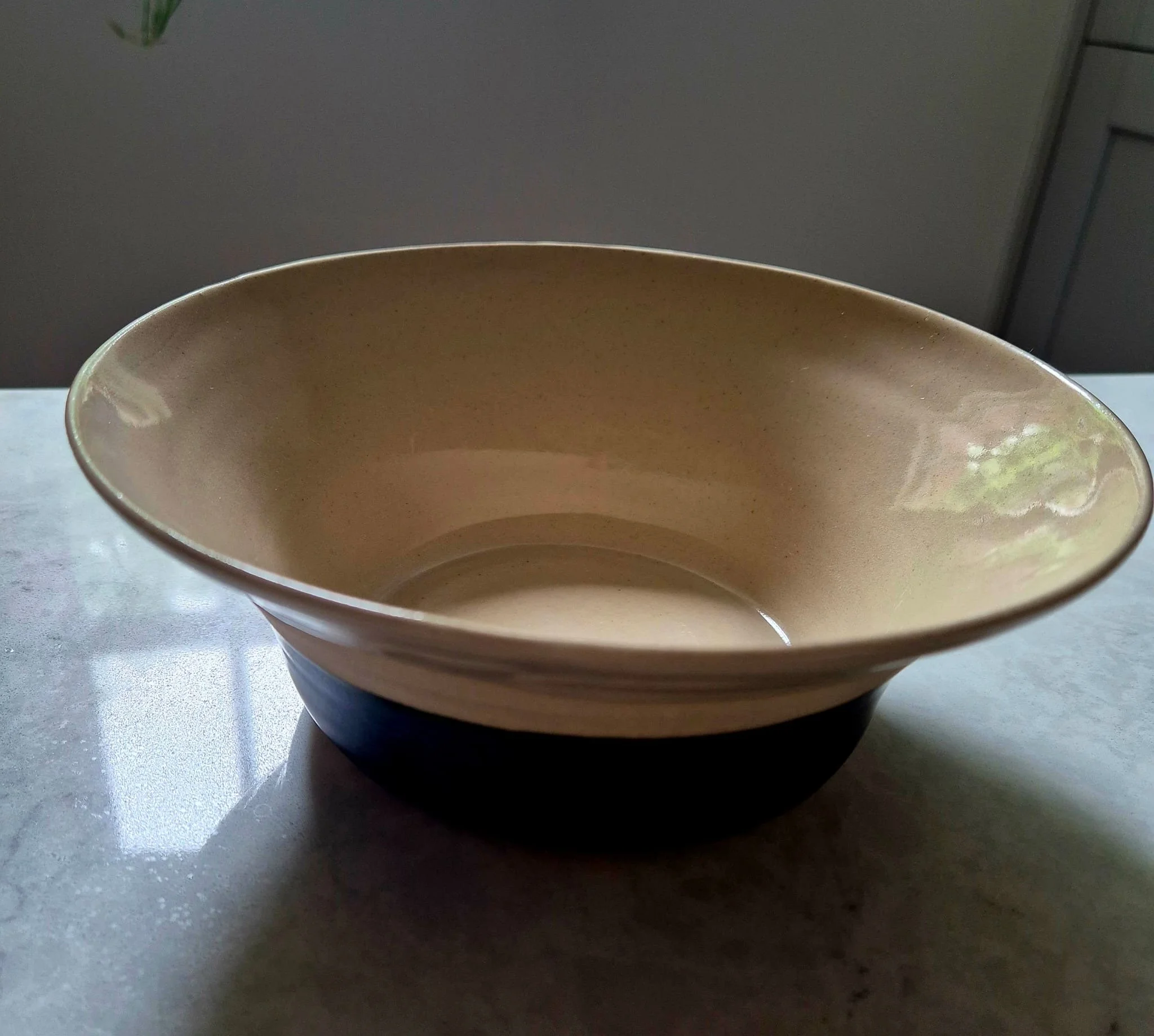 Empty beige ceramic bowl with a dark blue base on a reflective table