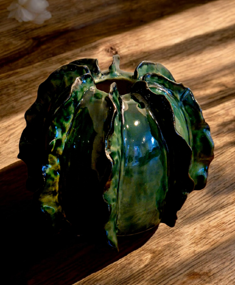 Glossy dark green ceramic vase with ruffled, leaf-like edges on a wooden table