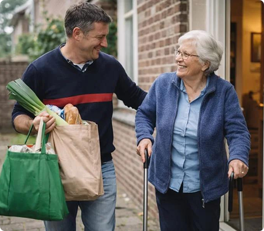 Smiling man carrying grocery bags and helping an elderly woman with a walker outside her home