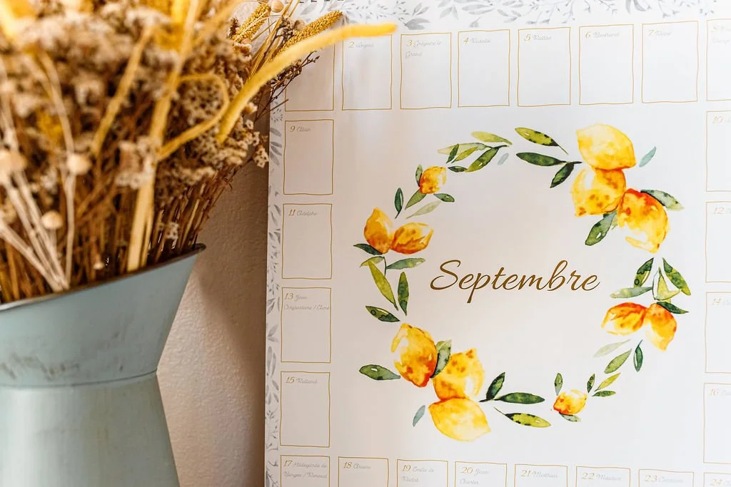 Calendrier mural de septembre décoré de fleurs jaunes peintes à l’aquarelle, à côté d’un bouquet de fleurs séchées dans un vase.
